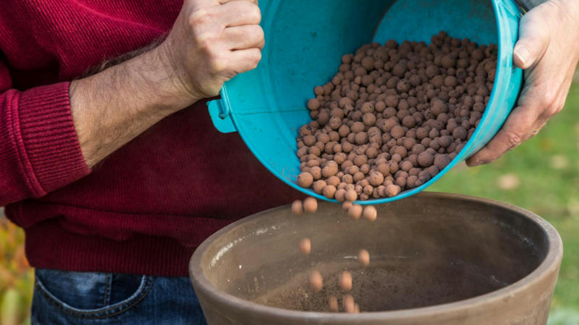 Jemand befüllt einen Blumentopf mit Blähton.