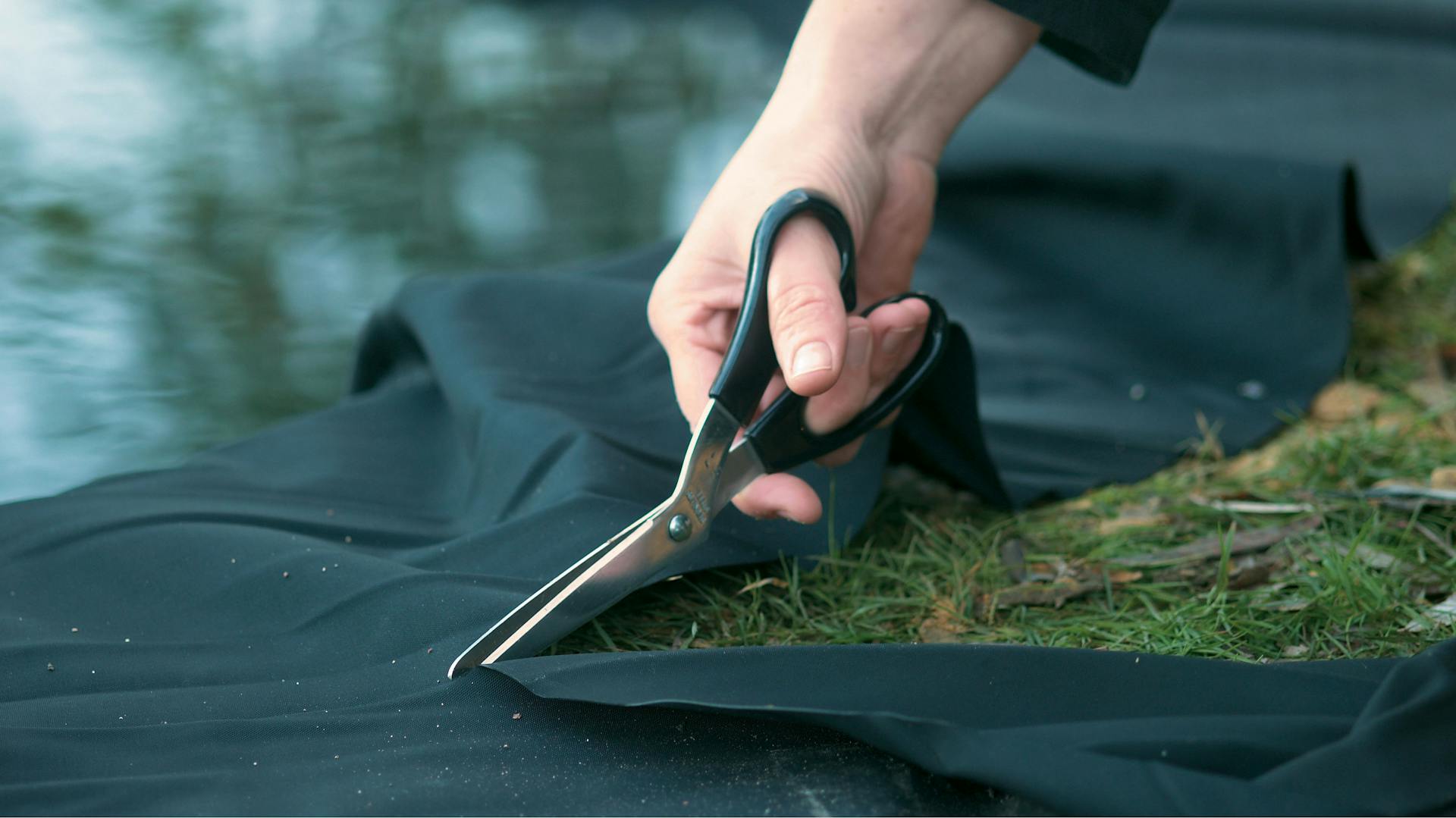 Jemand schneidet eine Teichfolie mit einer Schere zu.