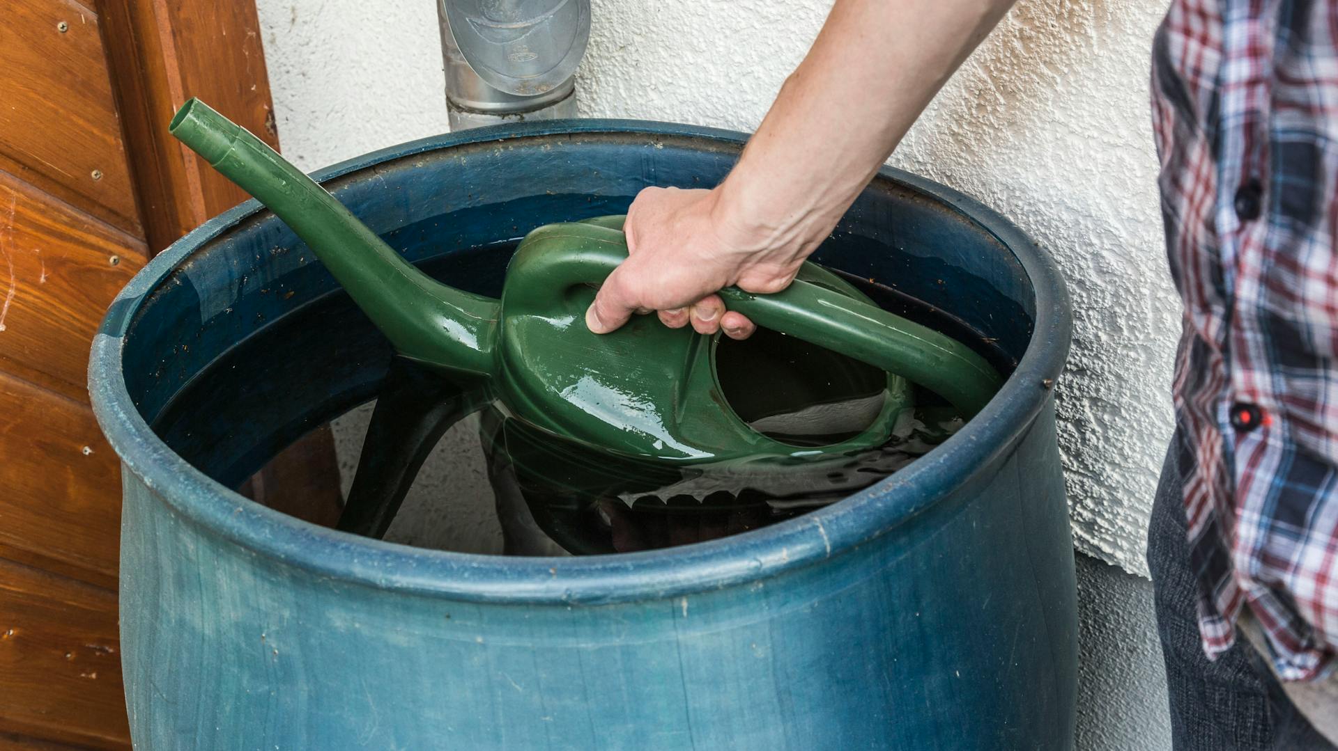 Una persona prende l’acqua da una cisterna per l’acqua piovana con un annaffiatoio.