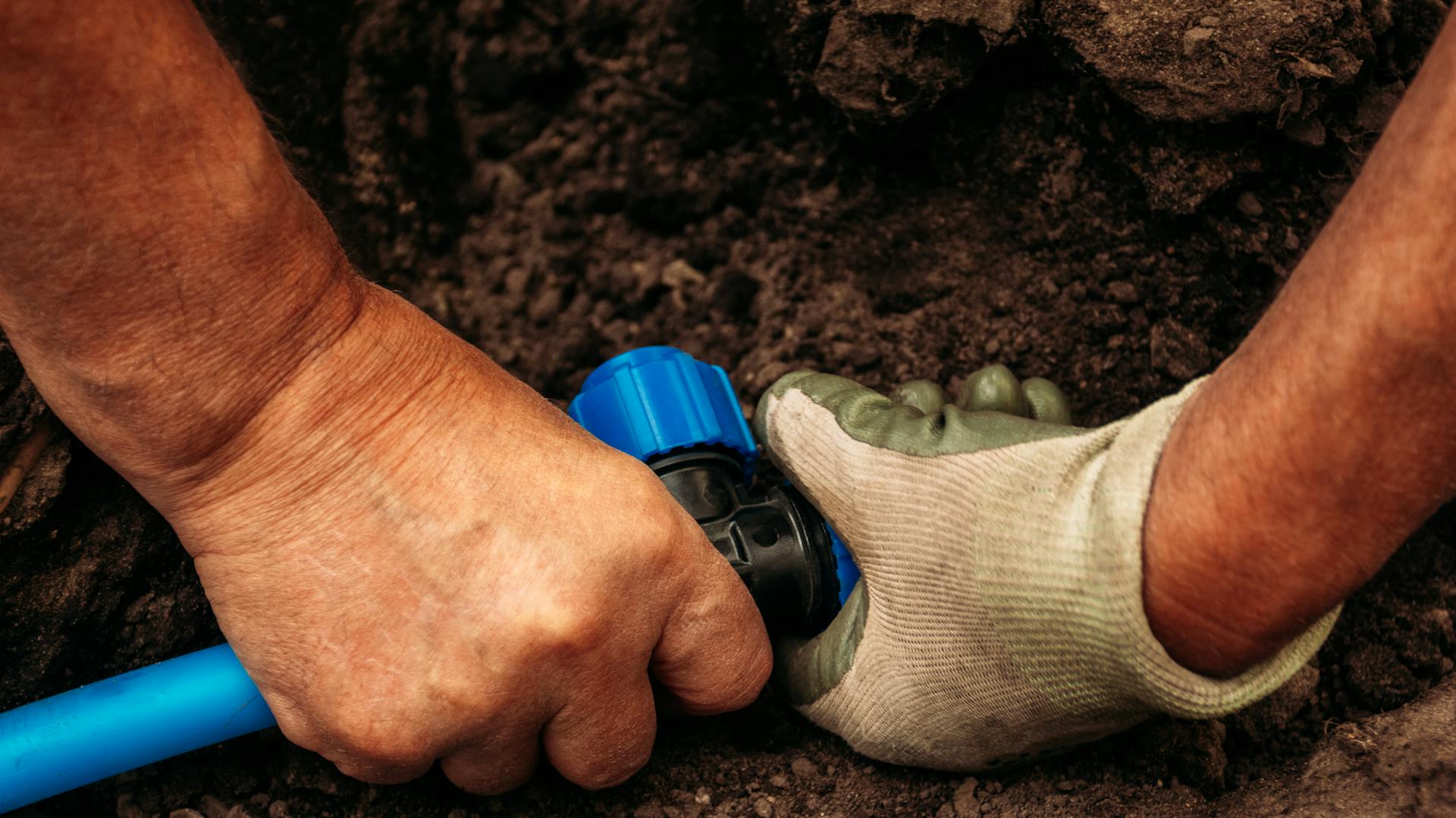 Una persona posa una tubazione dell’acqua nel terreno.