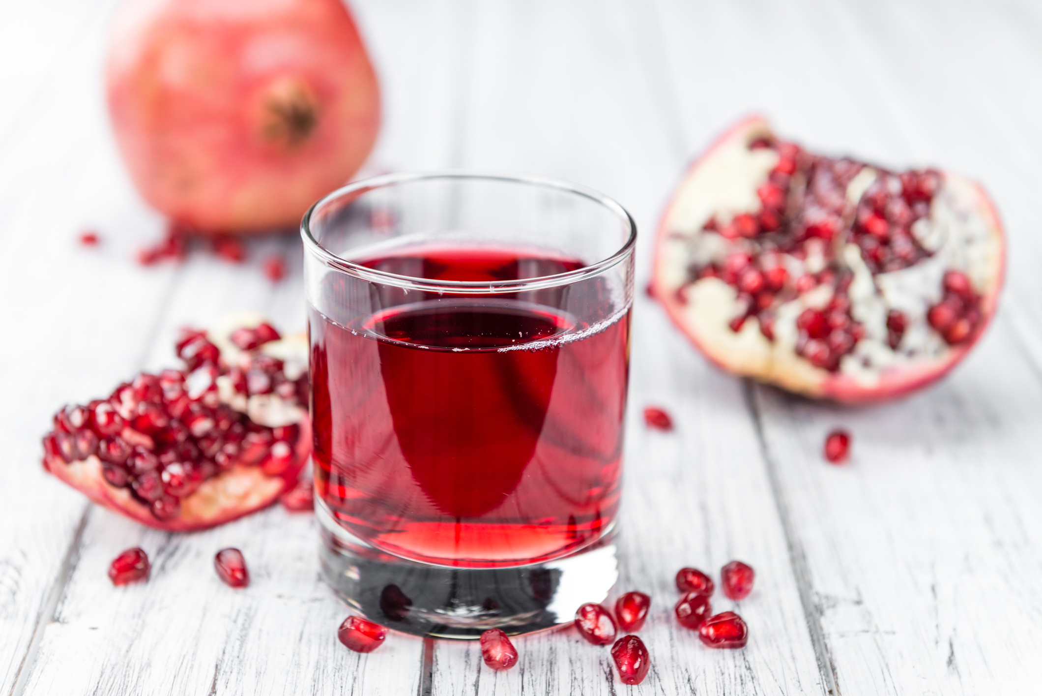 Granatapfelsaft im Glas vor einem geöffneten Granatapfel und vielen Kernen
