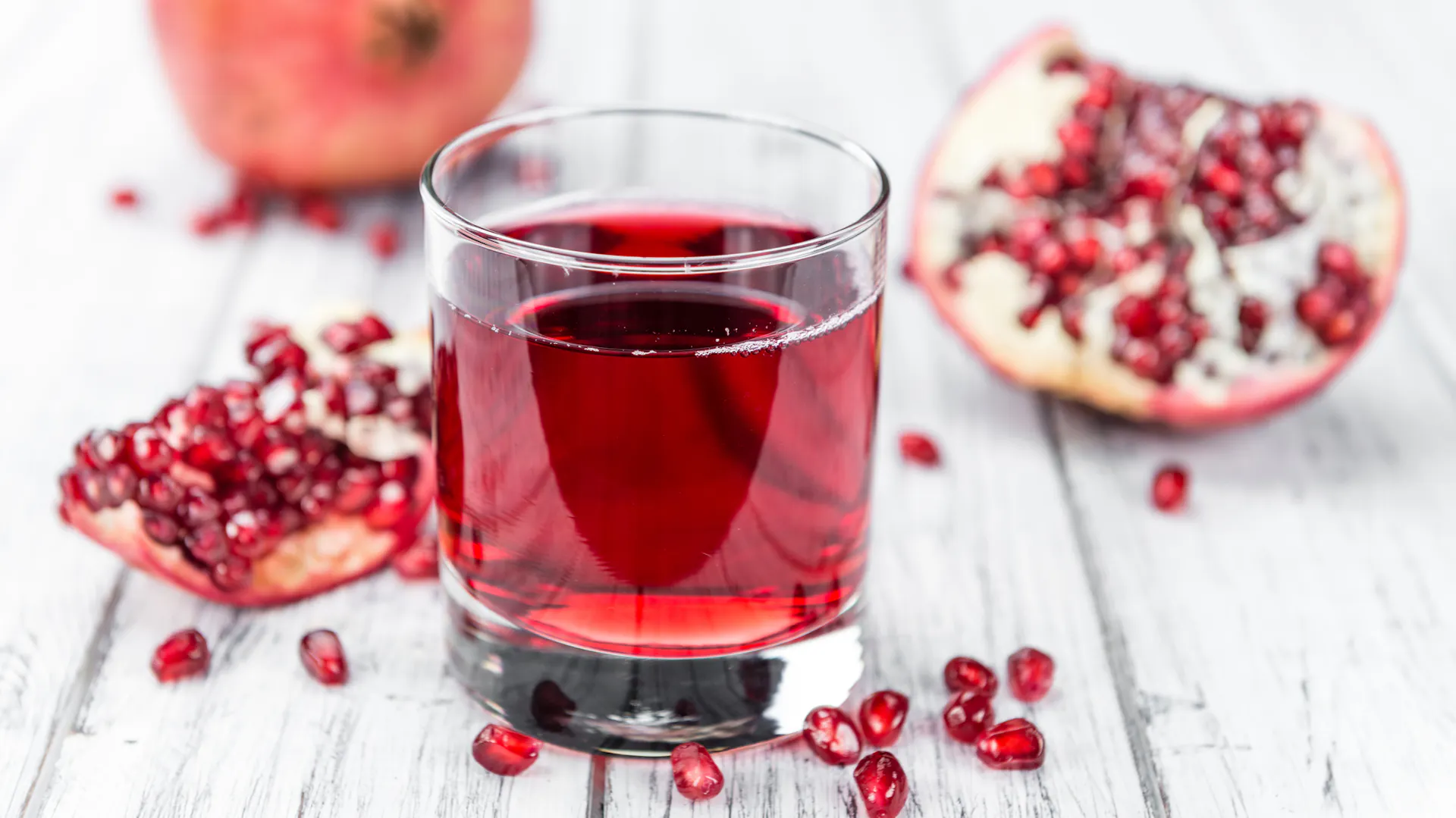 Granatapfelsaft im Glas vor einem geöffneten Granatapfel und vielen Kernen