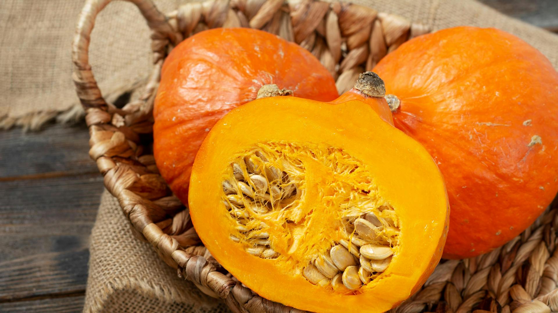 Zwei ganze und ein aufgeschnittener Hokkaido-Kürbis in einem Korb.