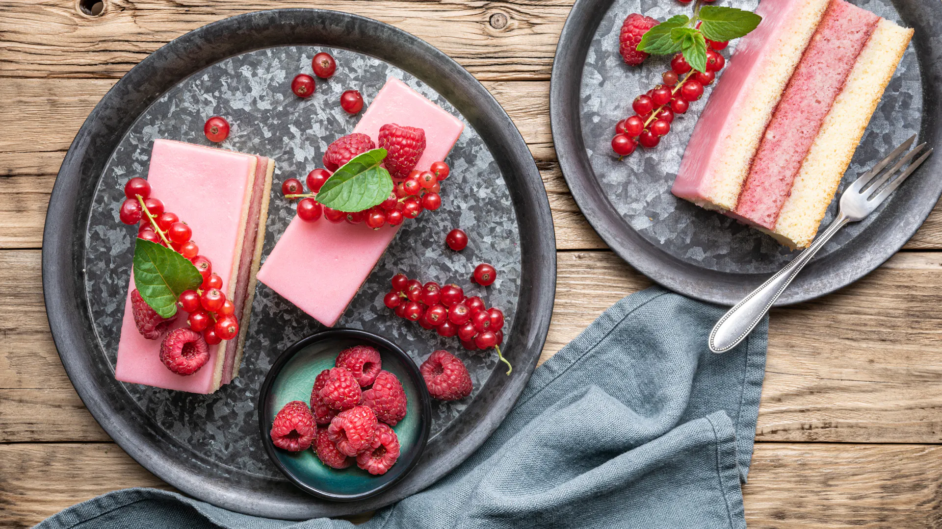 Johannisbeerkuchen liegt auf zwei Tellern garniert mit Himbeeren.