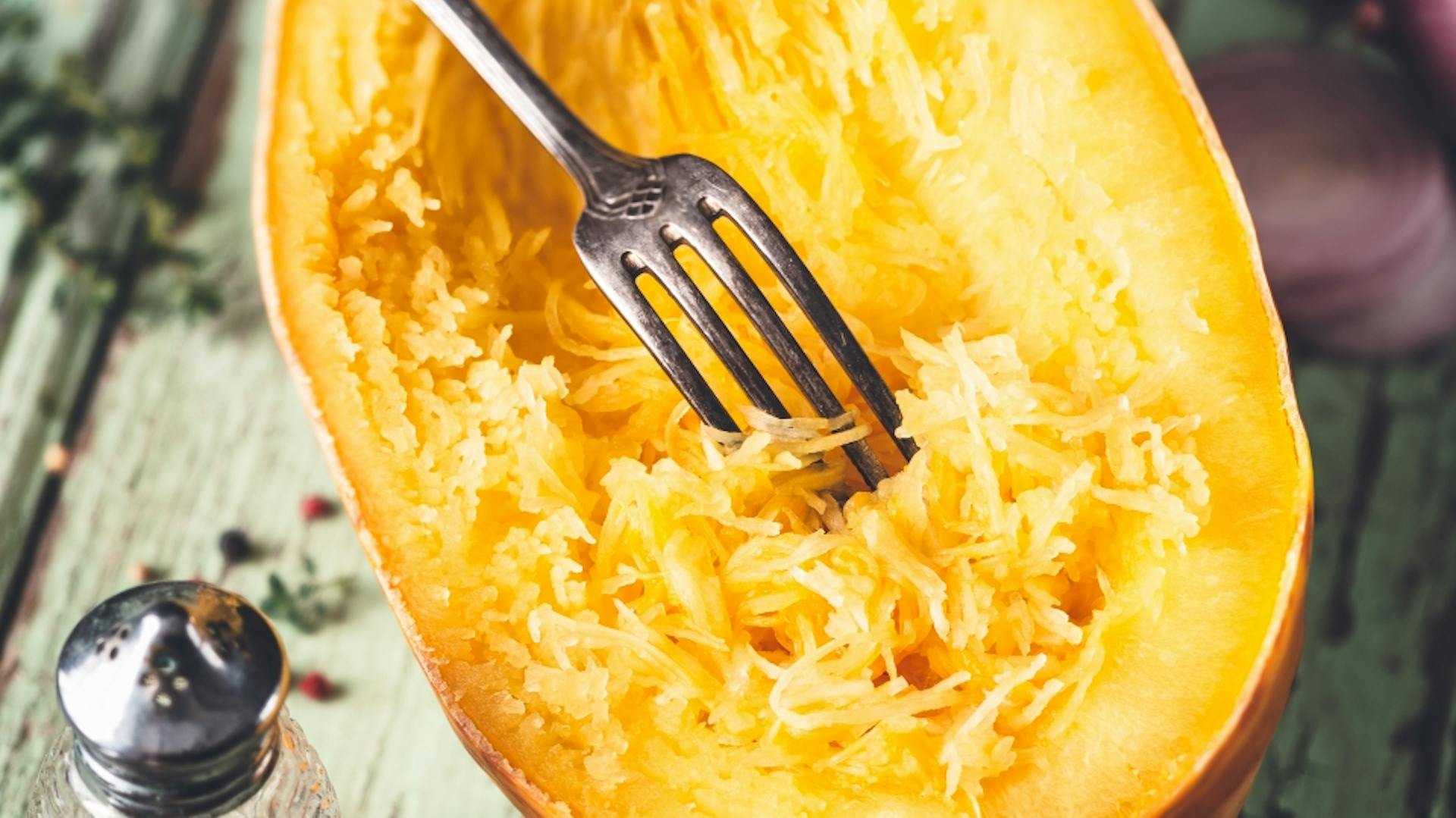 Gebackener, halbierter Spaghettikürbis mit durch eine Gabel aufgelockertem Fruchtfleisch.