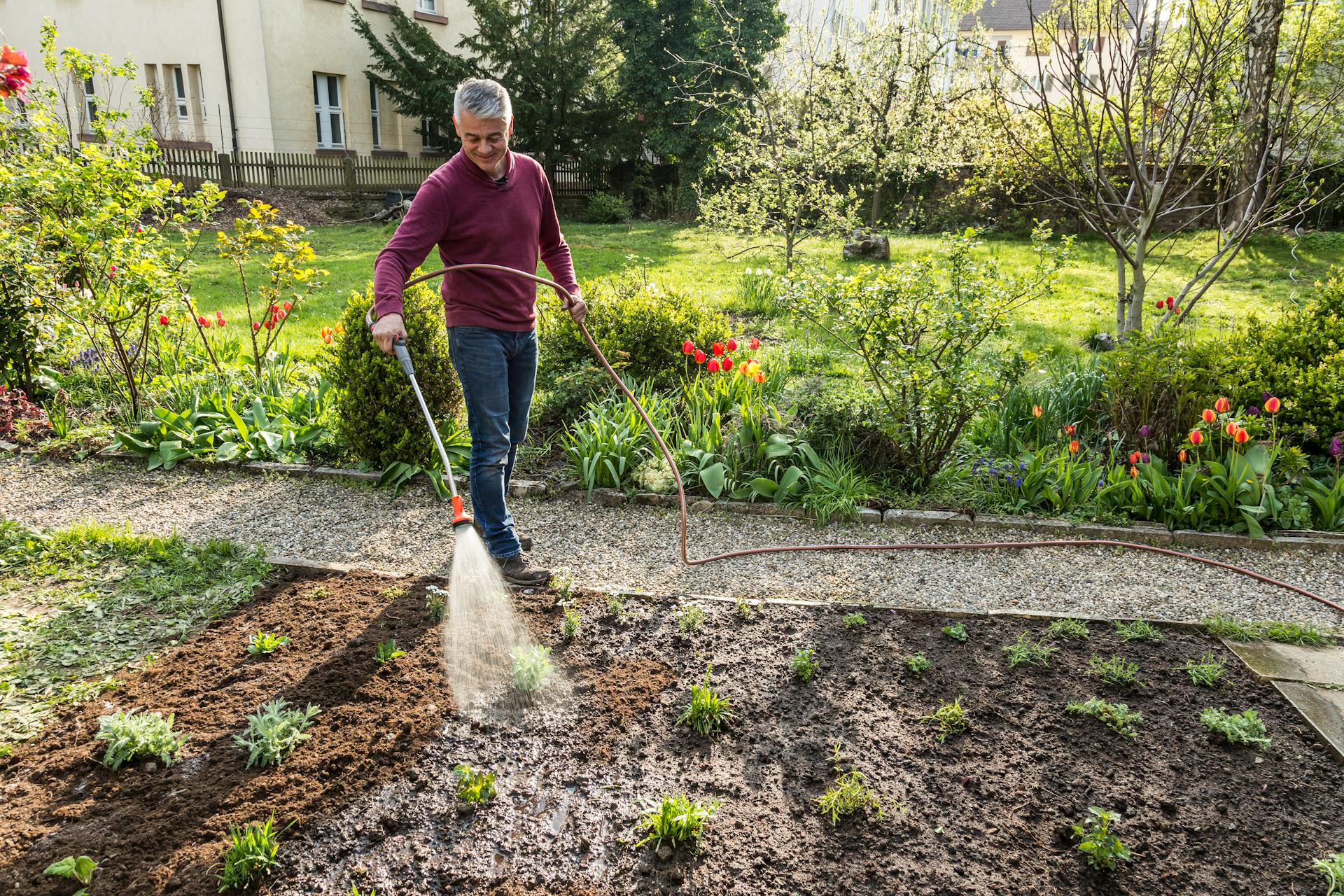 Una persona innaffia le piante nell’aiuola al sole del mattino.