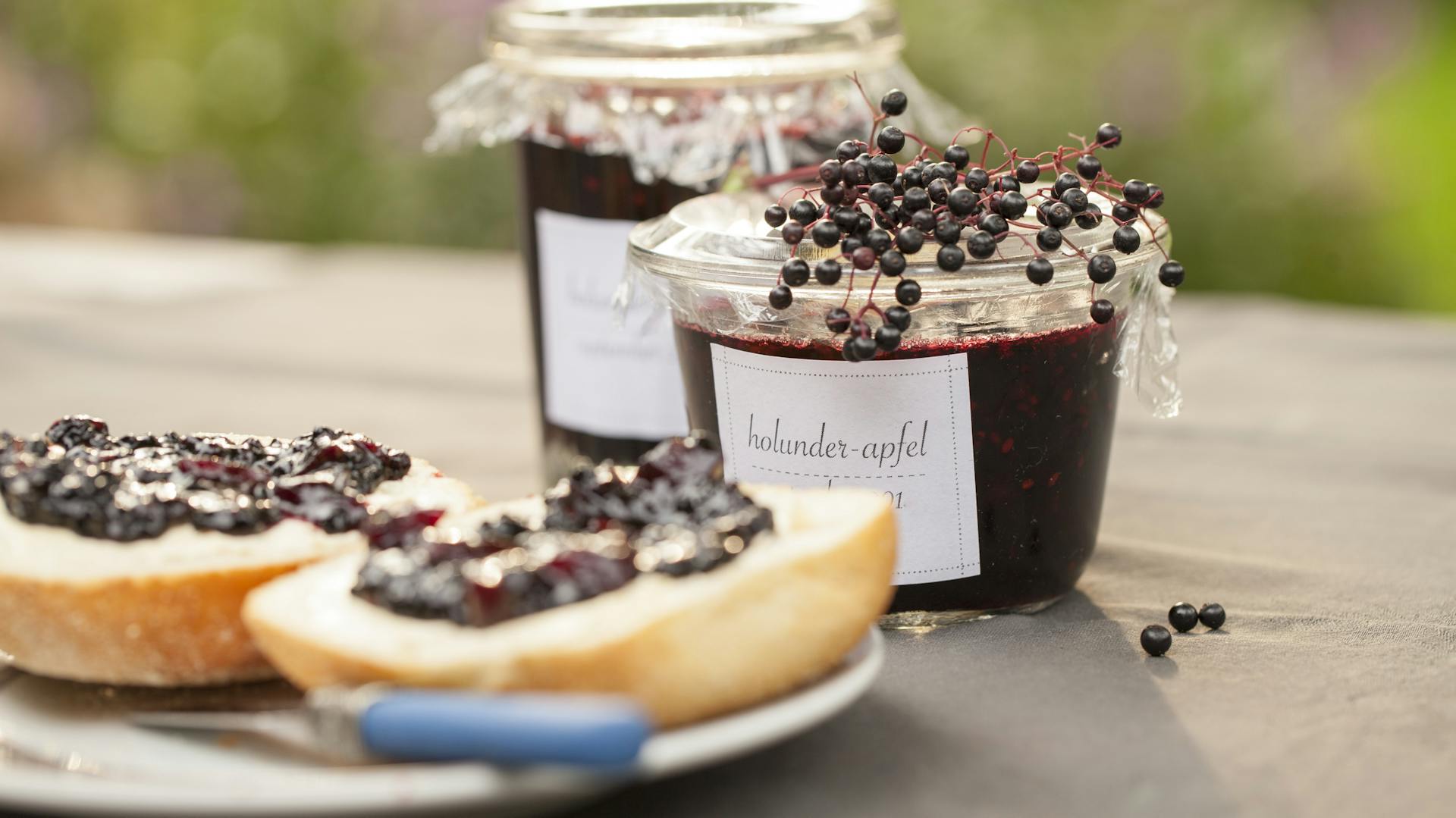 Holundermarmelade im Glas und auf dem Brötchen.