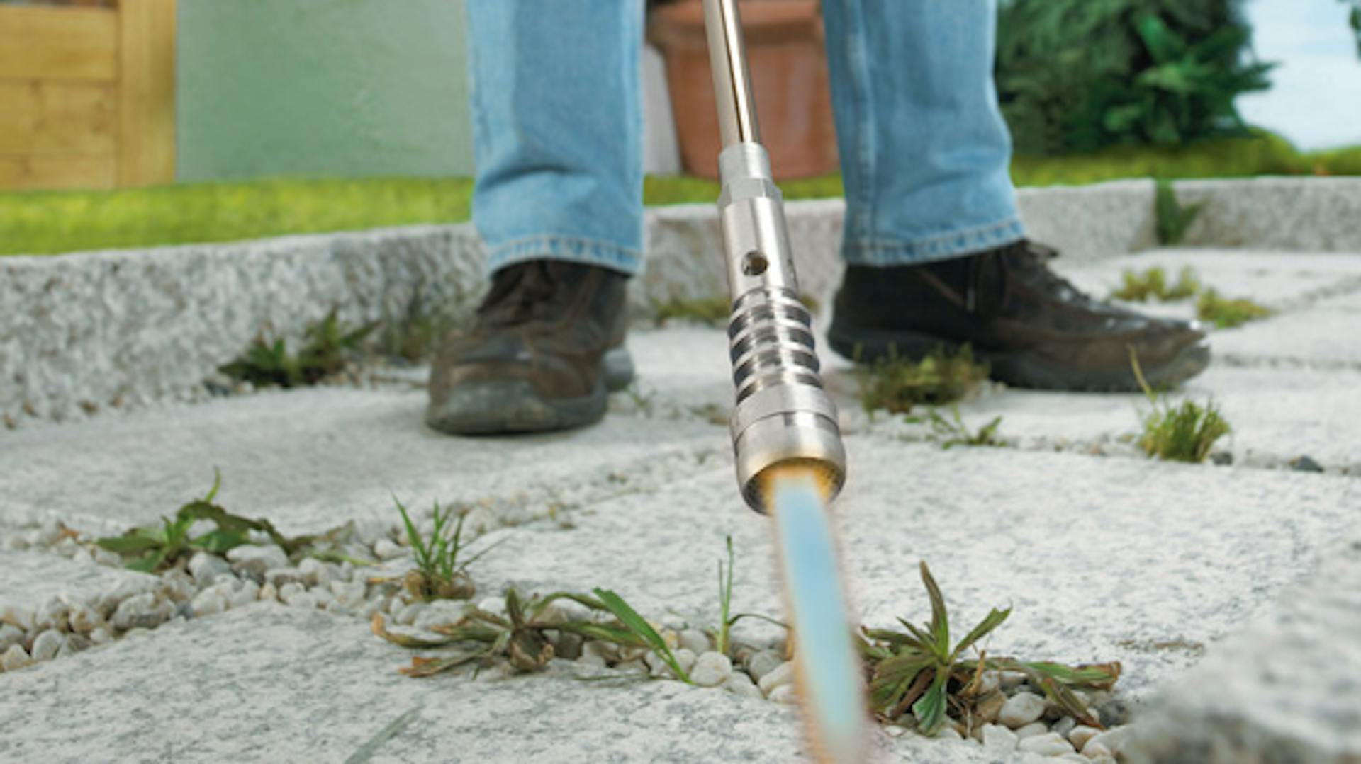 Jemand entfernt Unkraut aus Pflasterritzen mit einem Gasbrenner.
