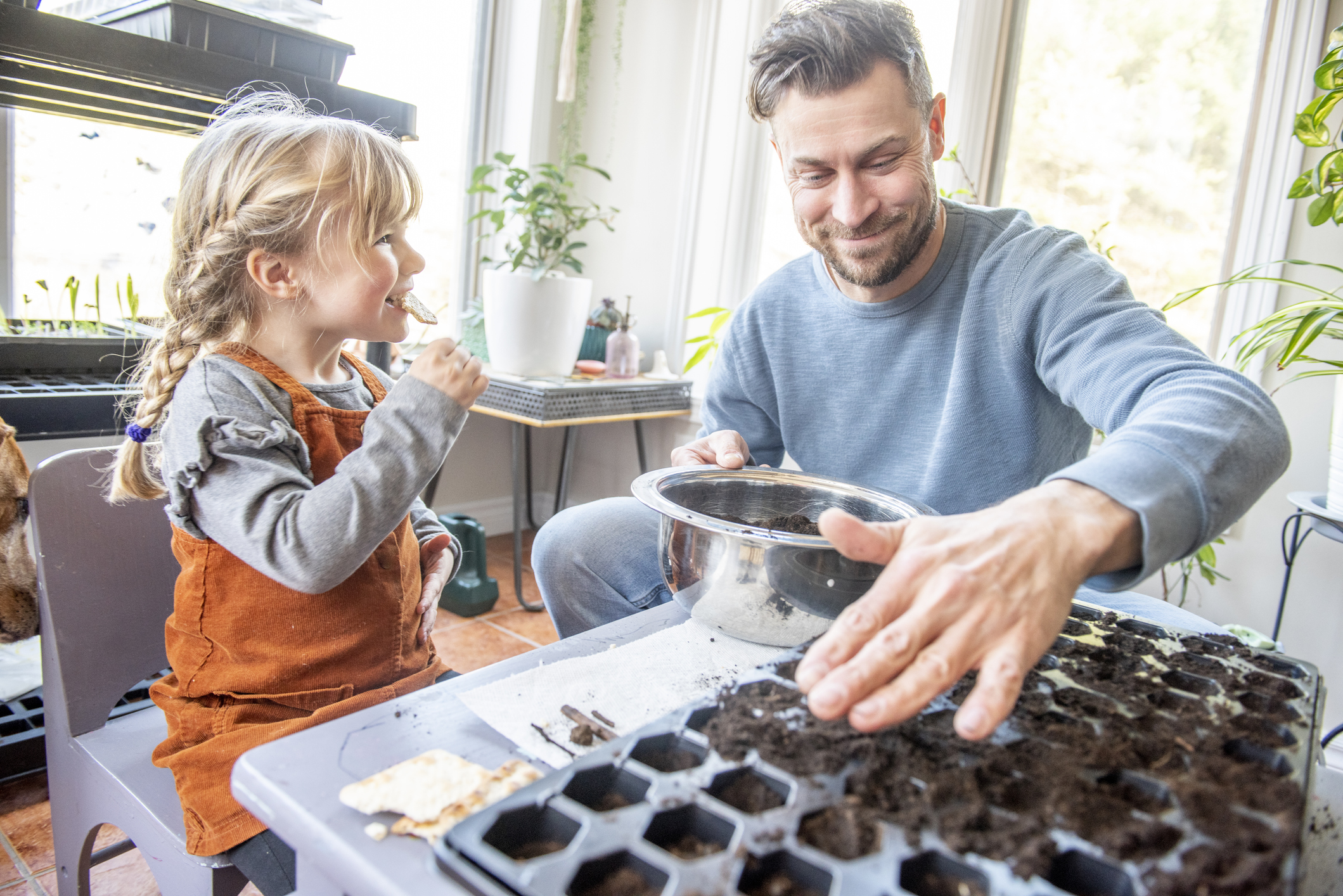 Eine Person füllt Erde in Anzuchttöpfe, ein kleines Kind sitzt daneben.