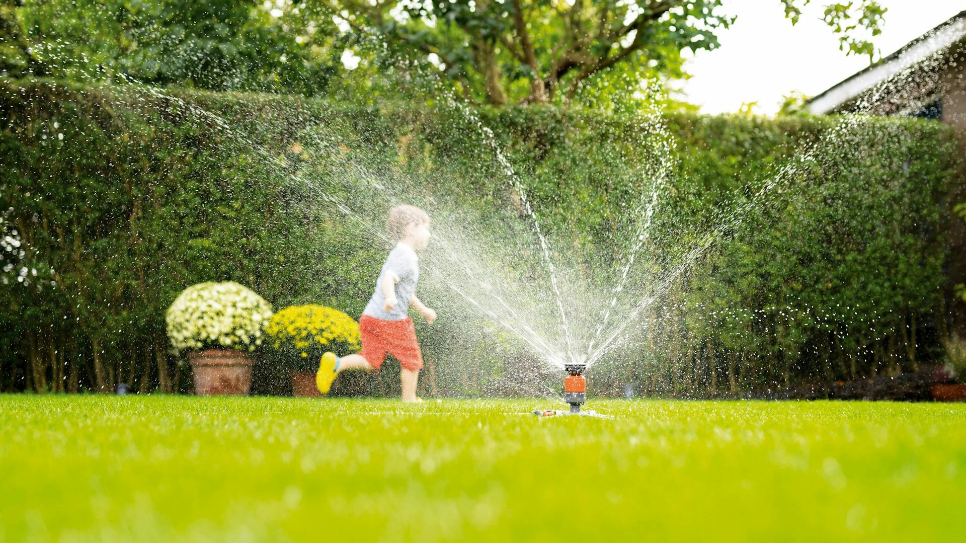 Kind rennt über den Rasen im Garten durch einen Rasensprenger
