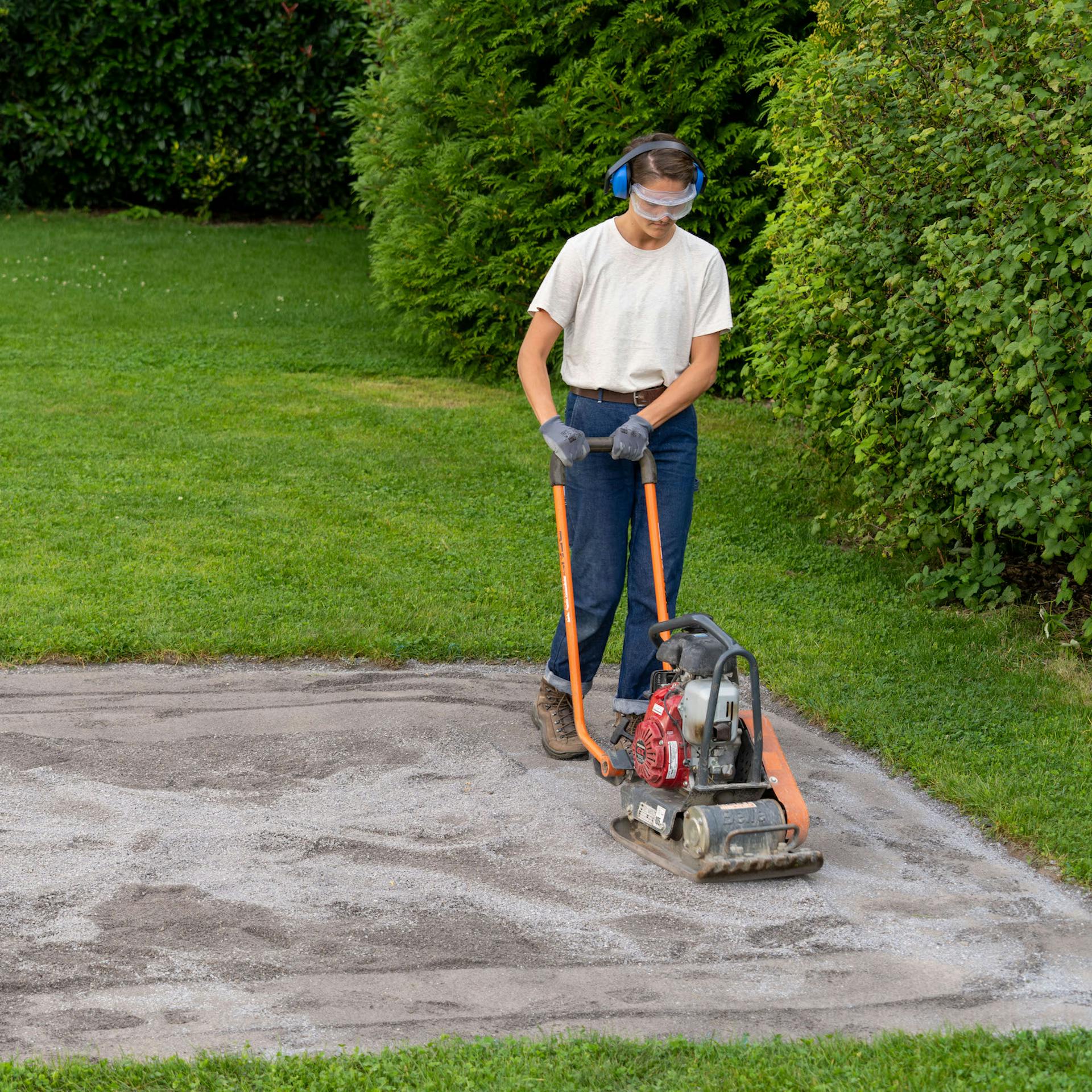 Žena projíždí vibrační deskou přes písčitou plochu