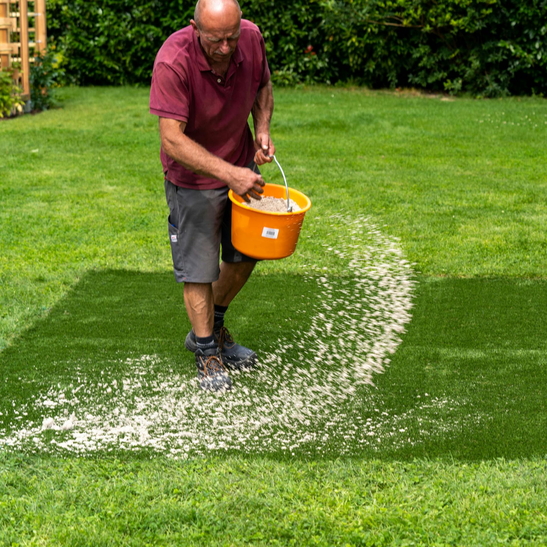 Muž rozhazuje písek po umělém trávníku