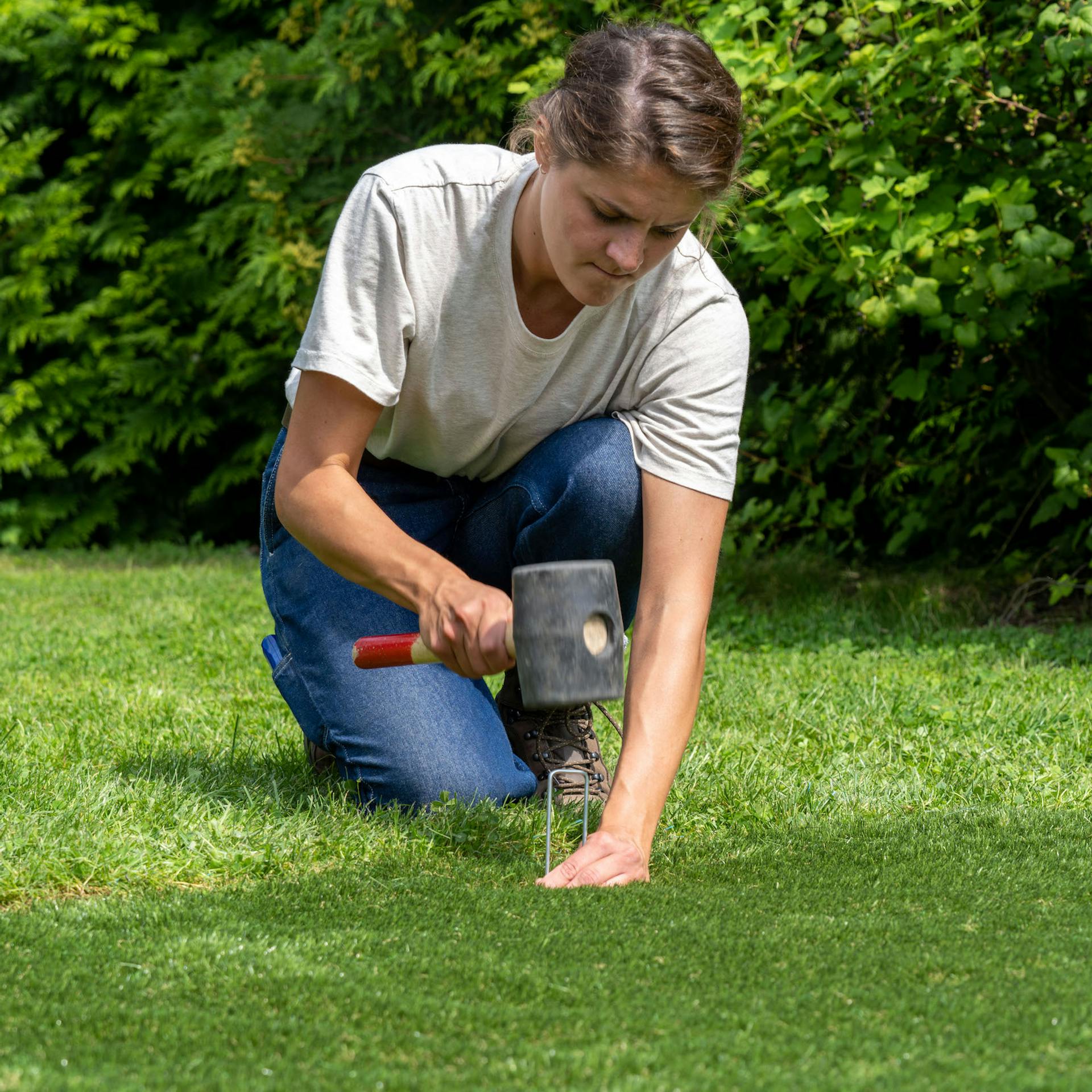Žena zatlouká palicí kovovou kotvu do trávníku