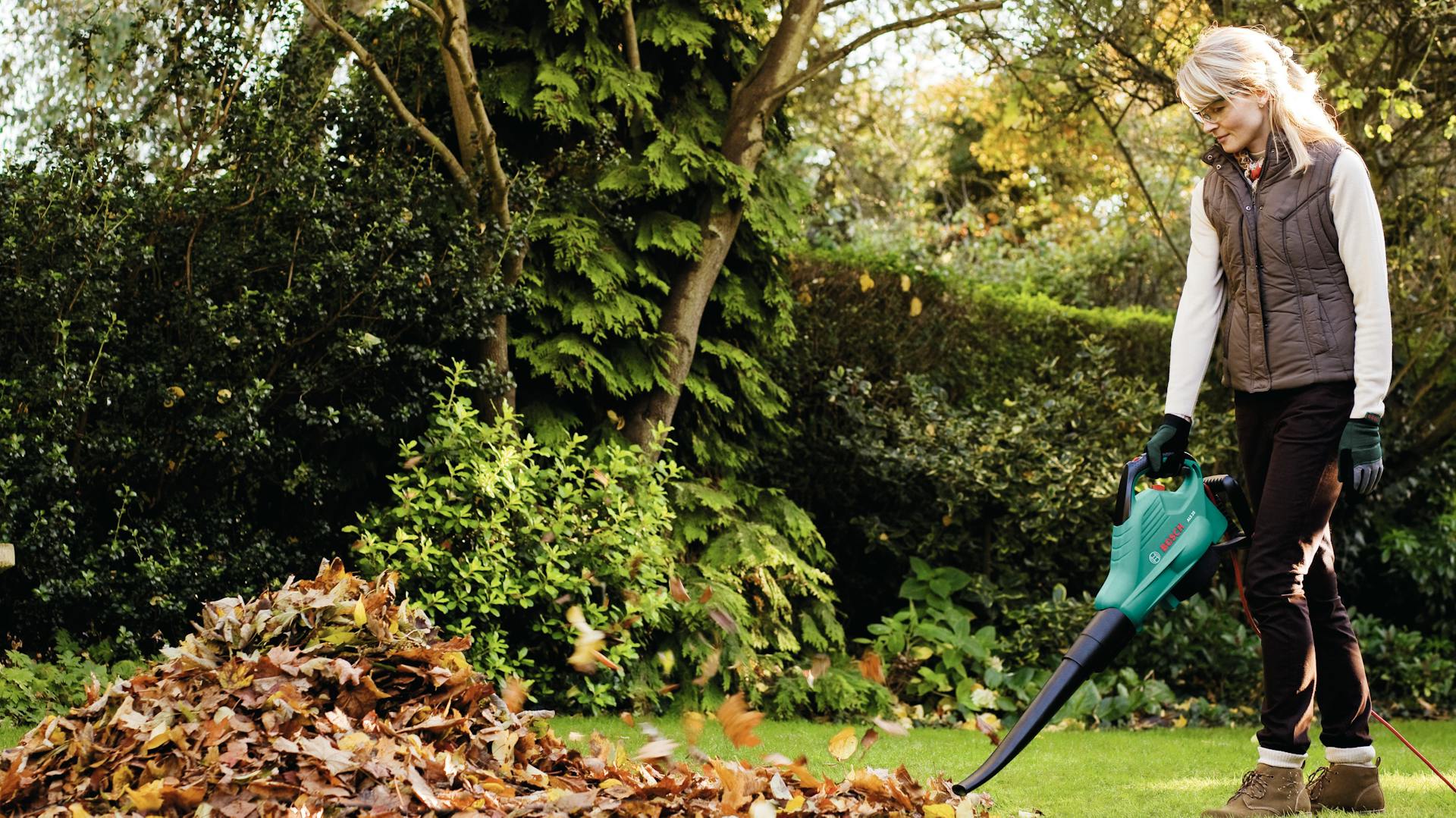 Frau bläst Laub vom Rasen.