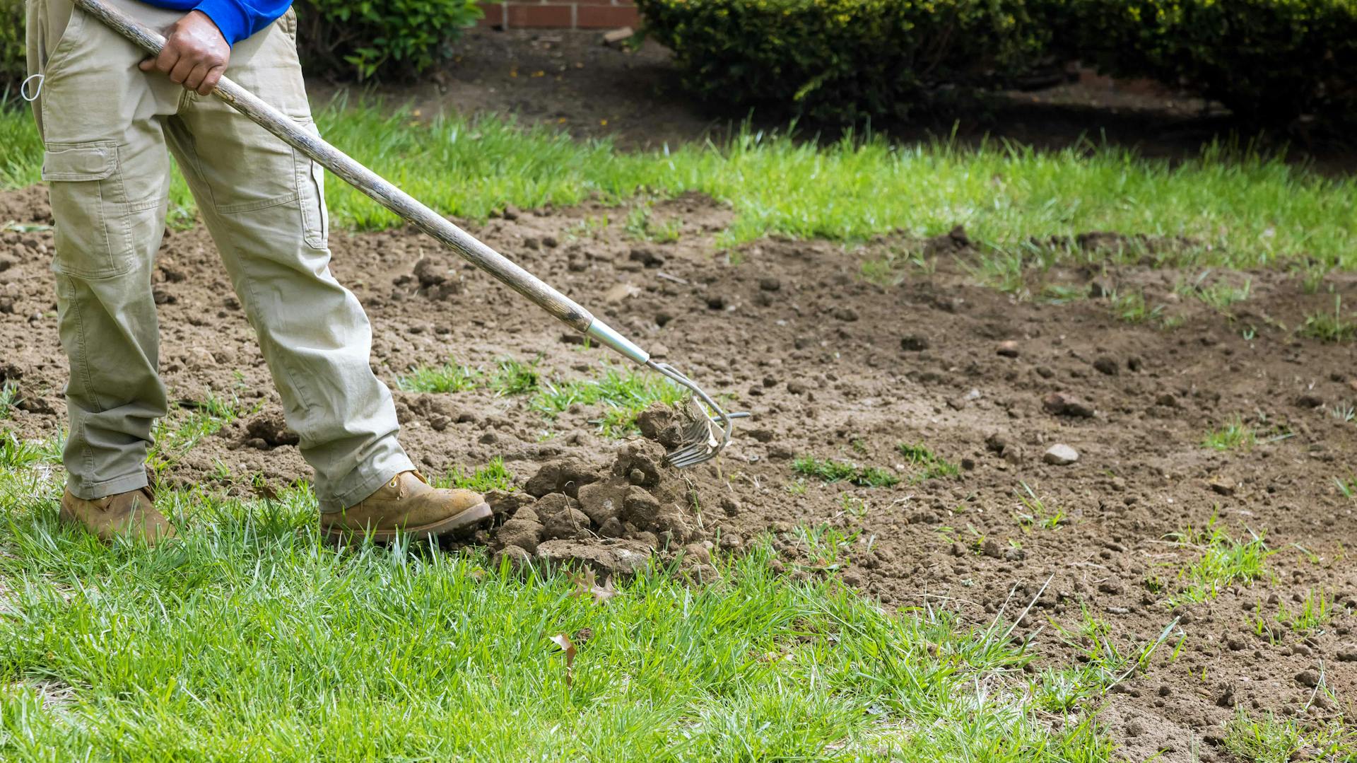 Valaki kapával készíti elő a területet egy kertben fűvetéshez.