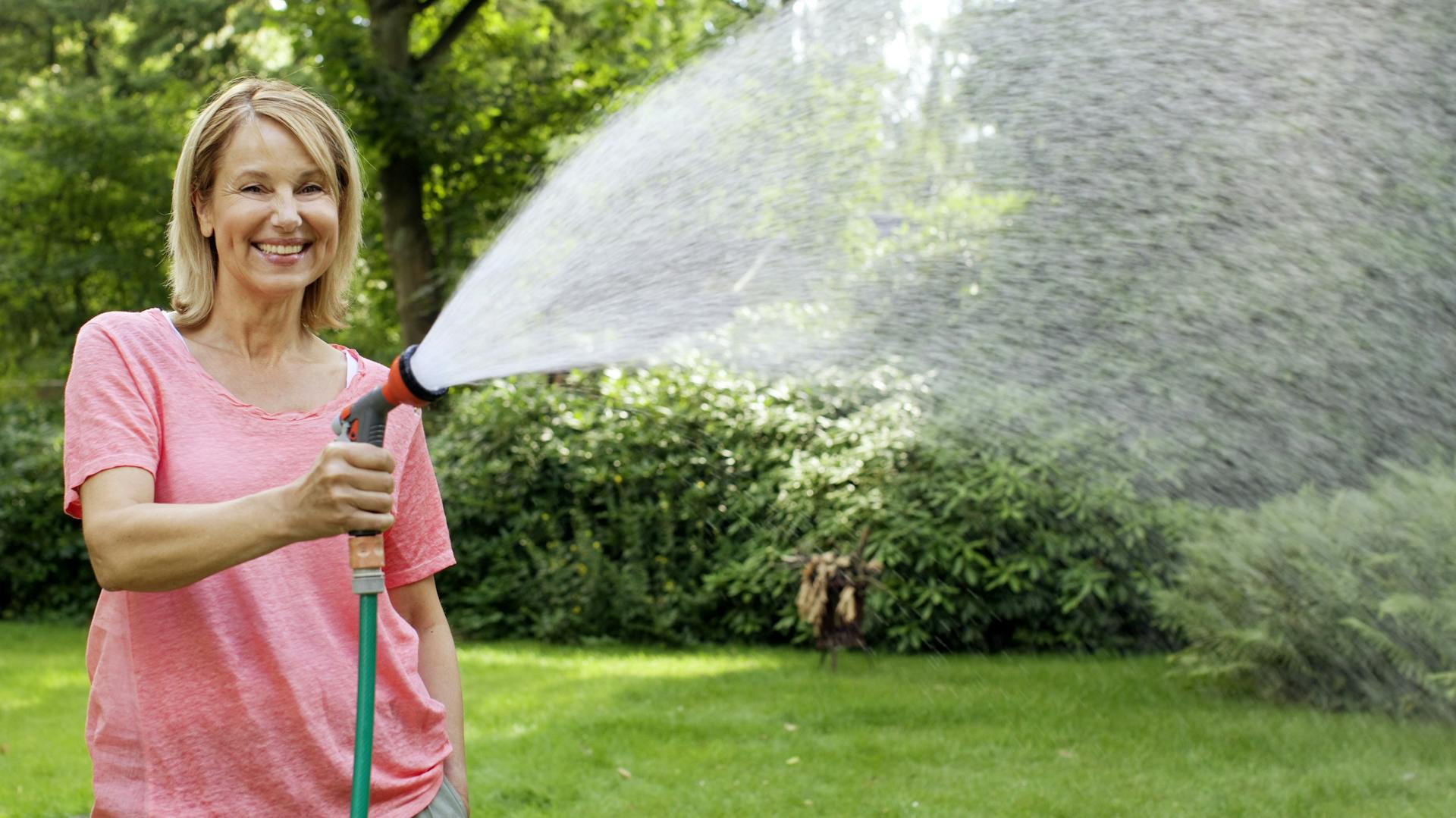 Egy nő slaggal öntözi a gyepet