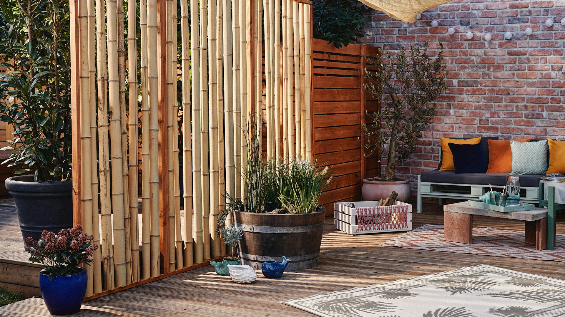 Terasa s bambusovou zástěnou, mini jezírkem, kamenným stolem a gaučem z palet.