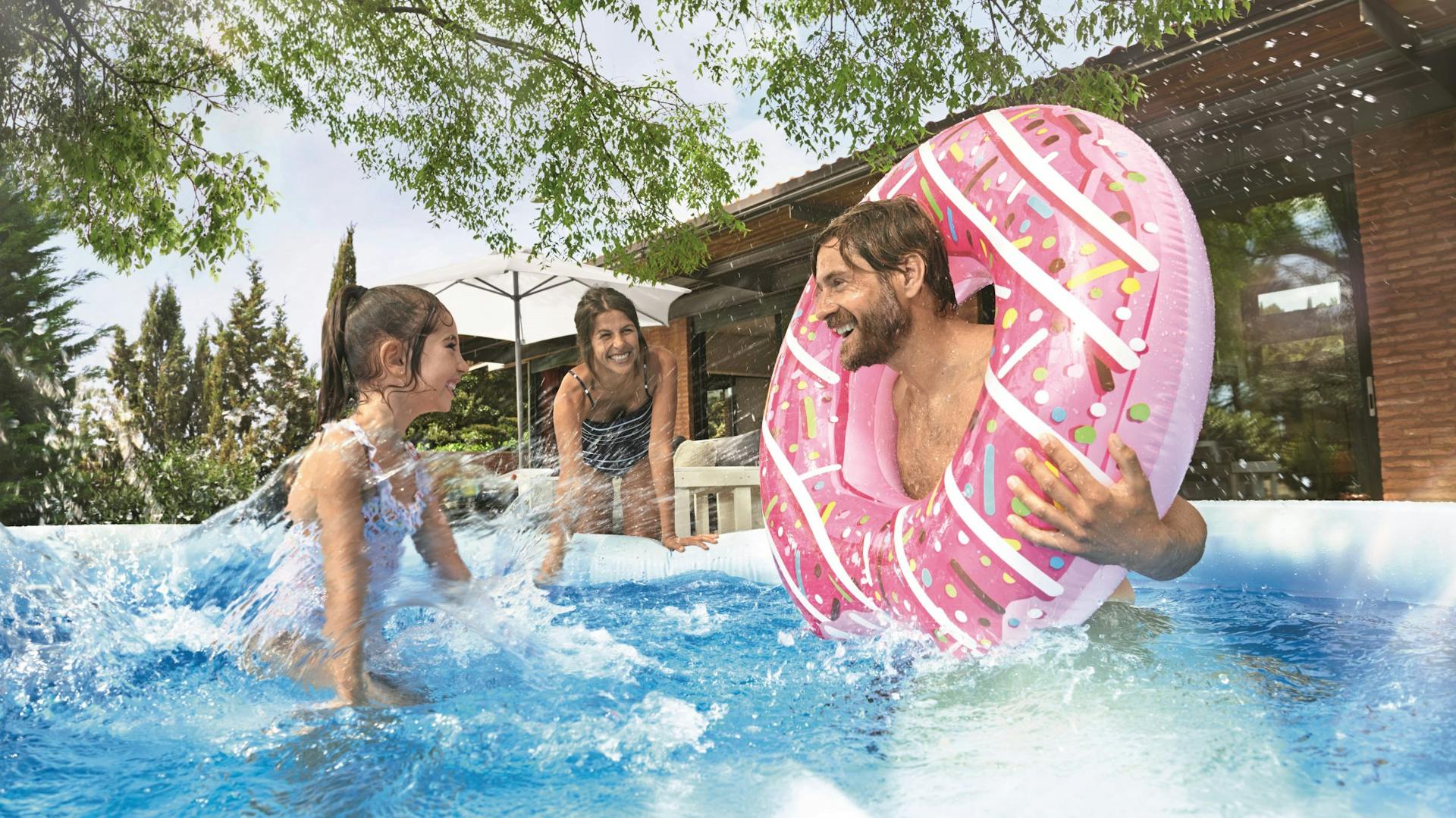 Familie spielt in Pool im eigenen Garten, Vater trägt einen pinken Schwimmring