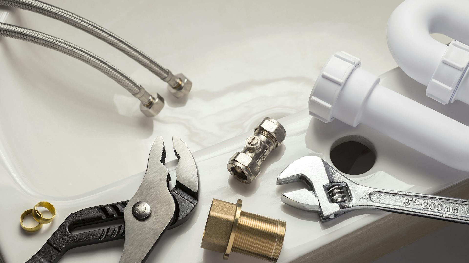 Diverse Werkzeuge zur Sanitärinstallation liegen auf einem Waschbecken