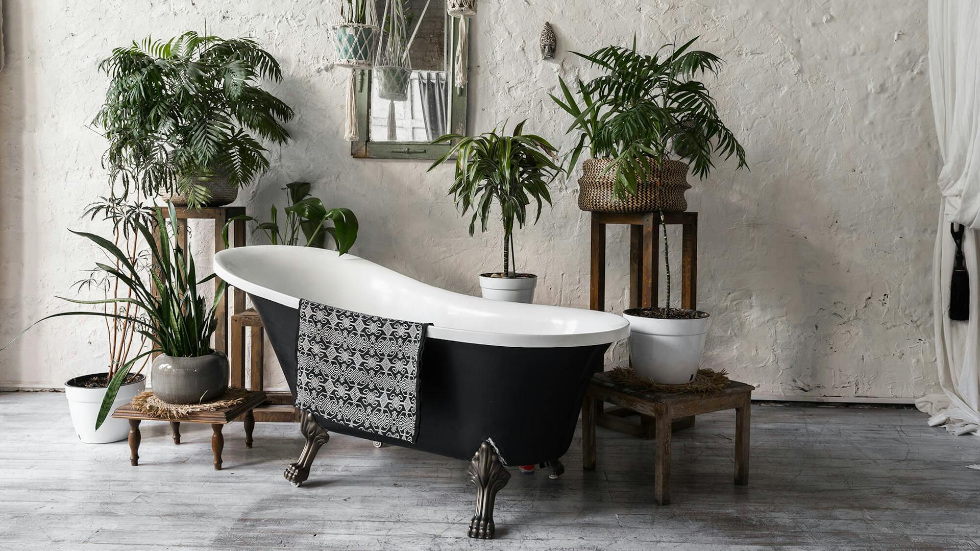 Schwarze freistehende Badewanne umgeben von Pflanzen.