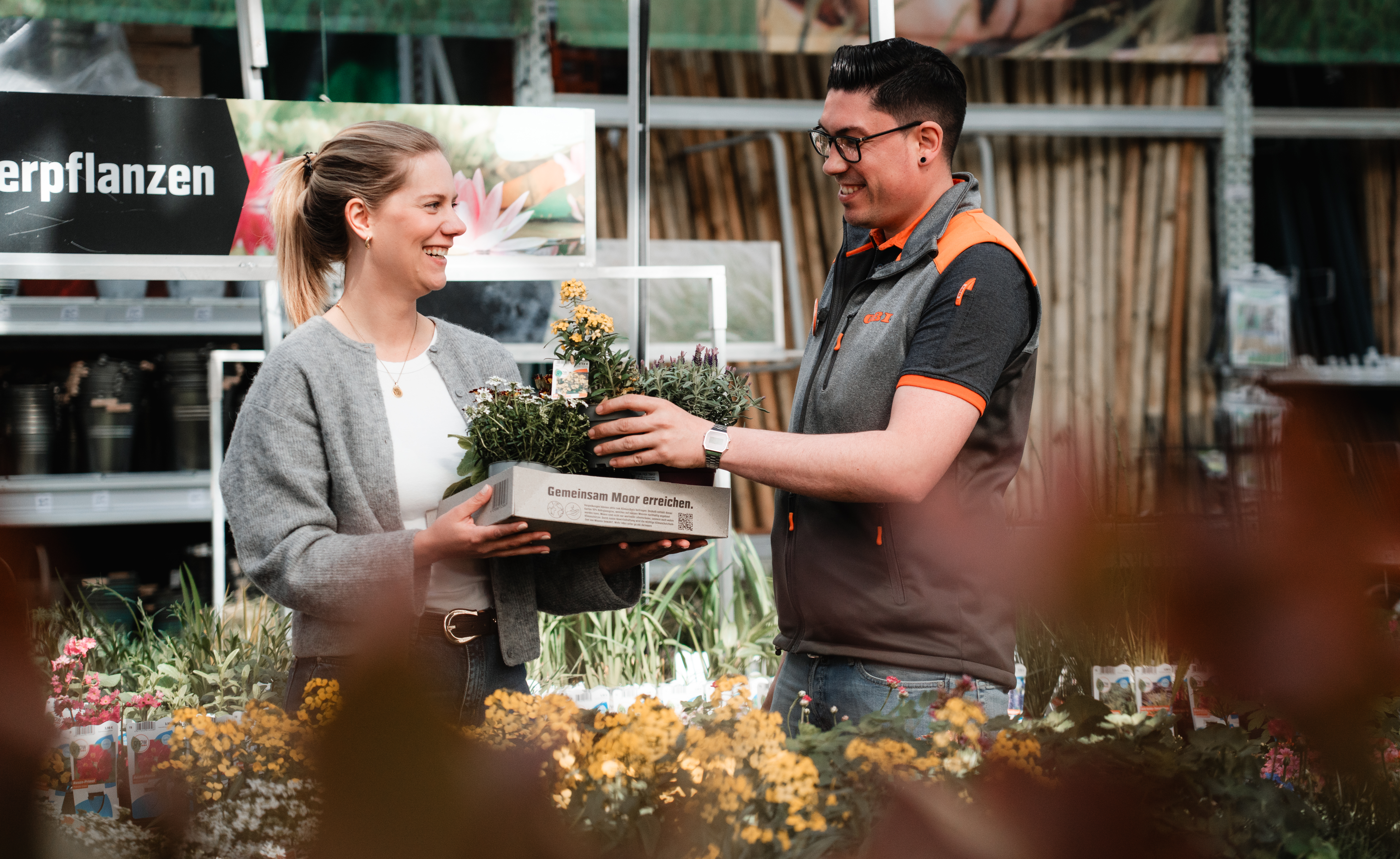 Marktmitarbeiter befüllt Paludi Karton einer Kundin mit Pflanzen