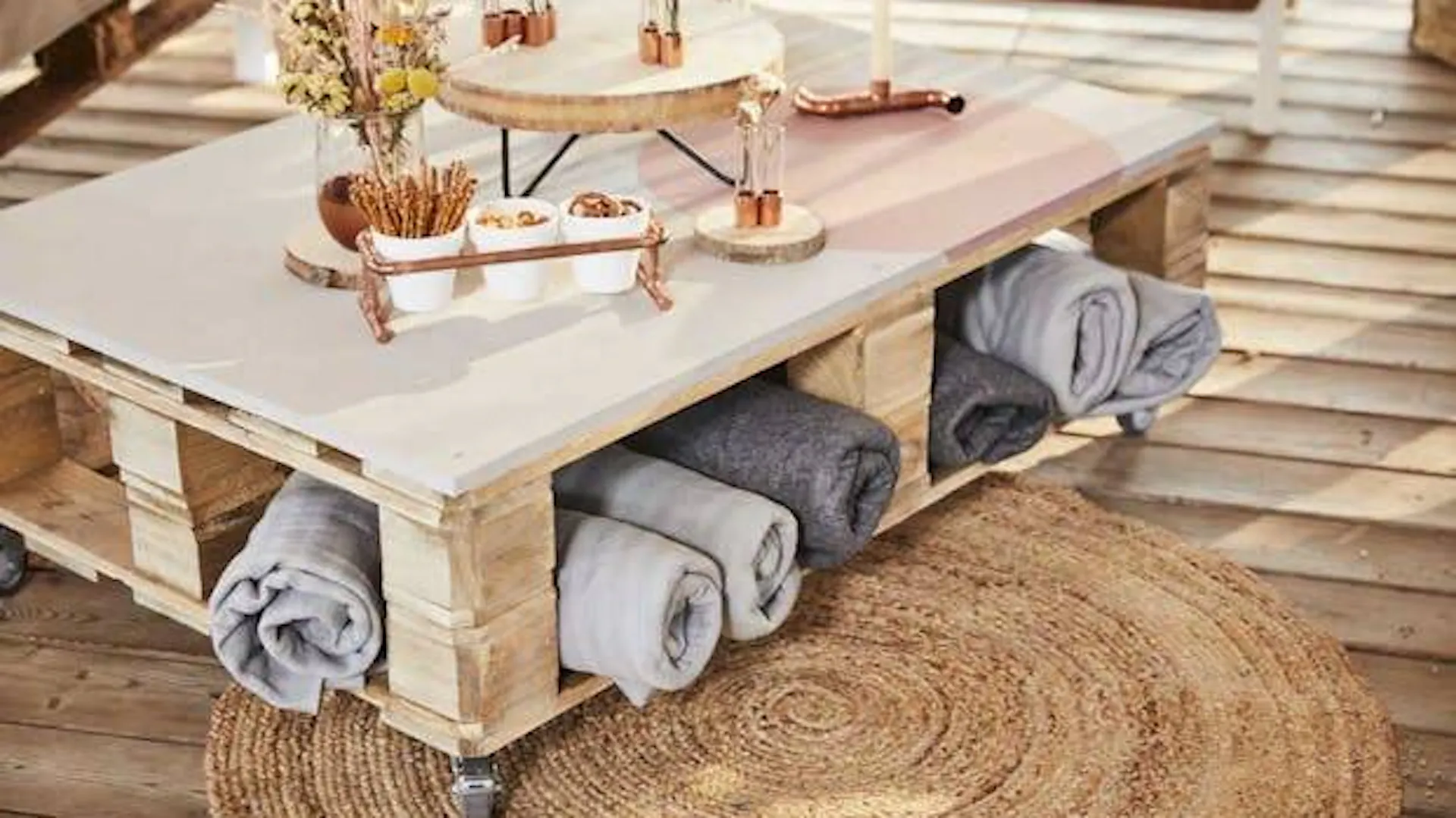 Stolik drewniany na kółkach stoi na plecionym dywanie – wystrój tarasu w stylu boho