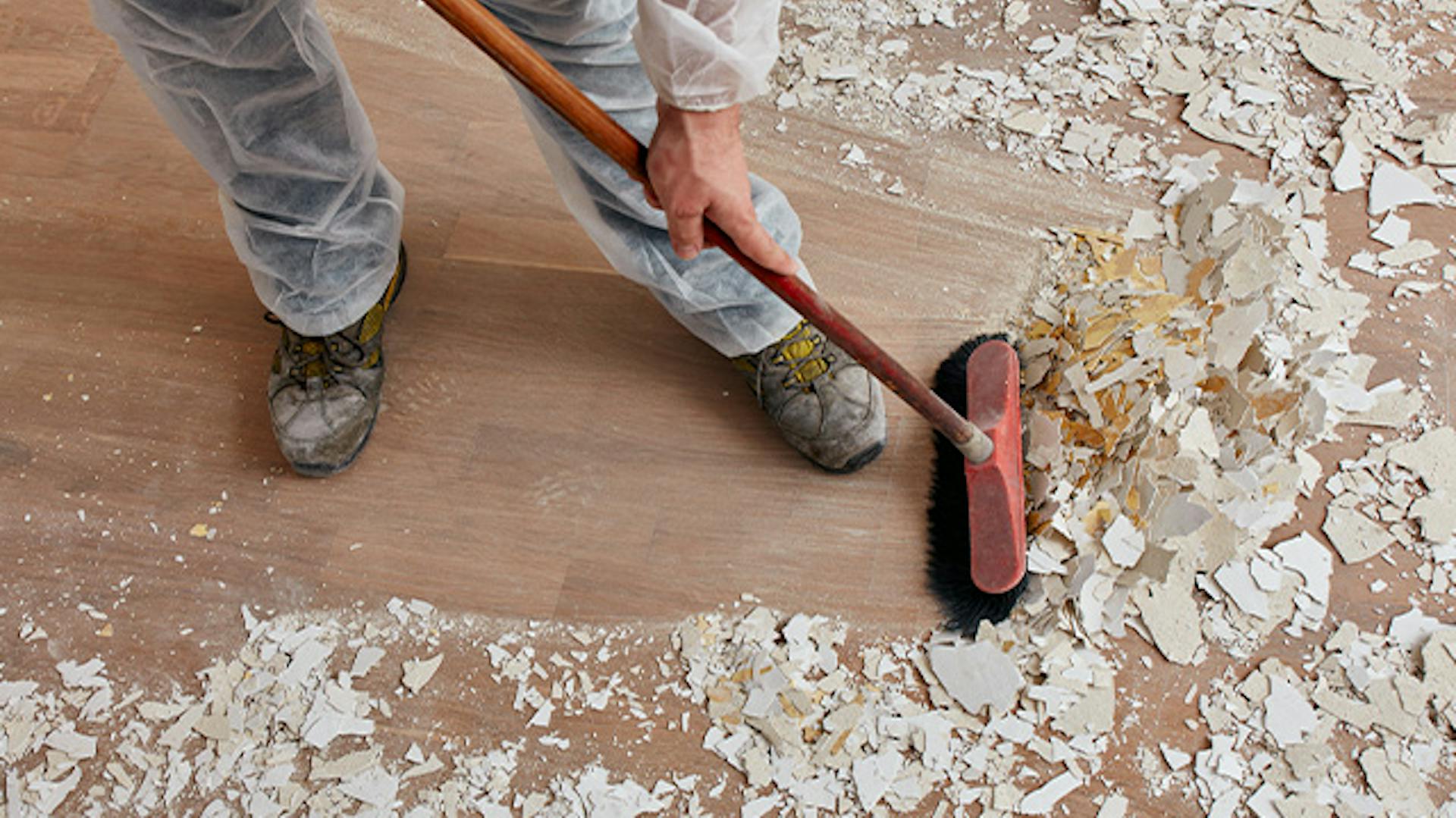 Mężczyzna zamiata miotłą resztki tynku i farby.