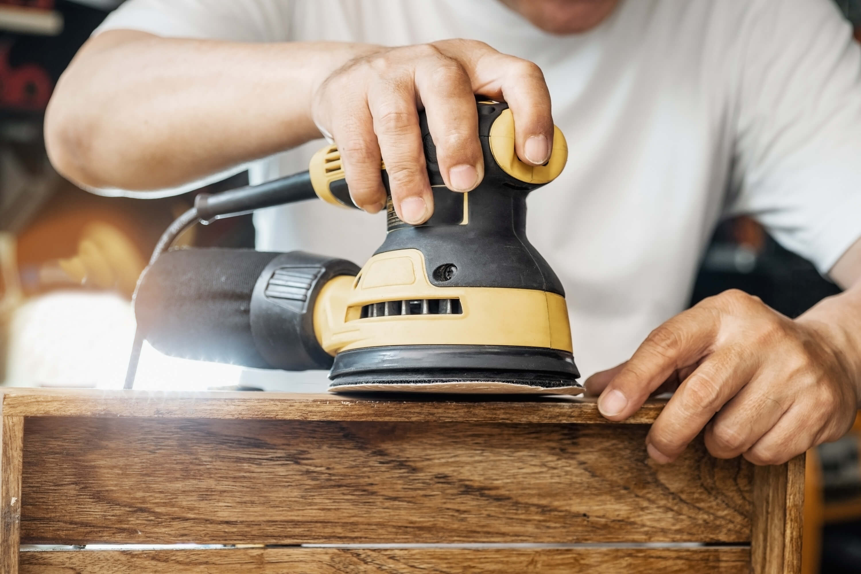 Mężczyzna szlifuje drewniany element elektryczną szlifierką mimośrodową.