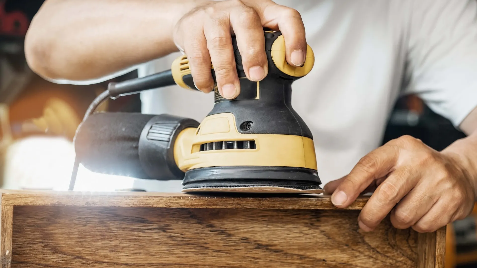 Mężczyzna szlifuje drewniany element elektryczną szlifierką mimośrodową.