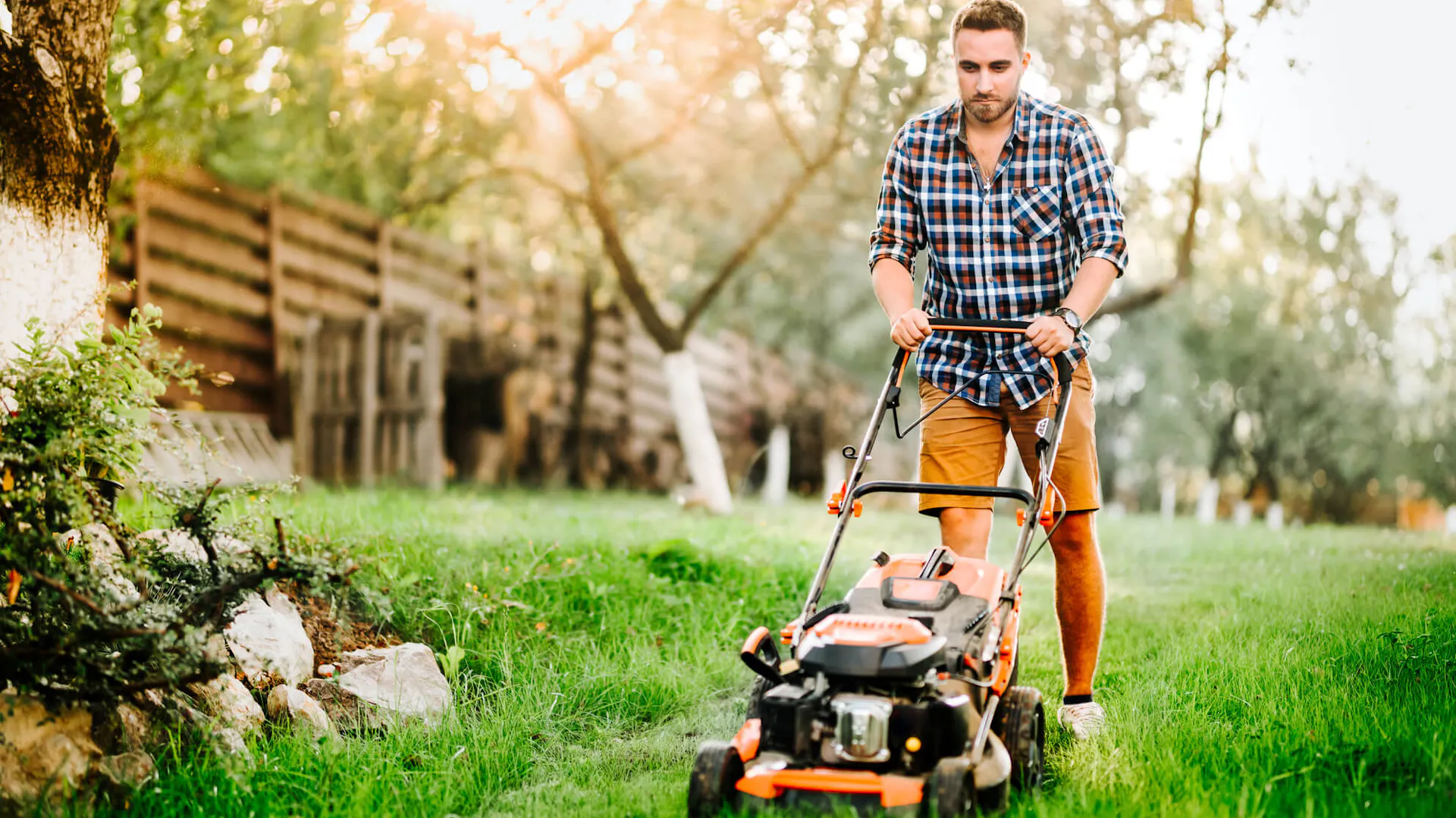 Młody mężczyzna kosi trawę kosiarką spalinową