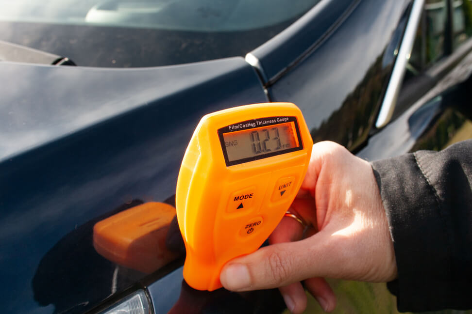 Mężczyzna używa miernika lakieru, aby sprawdzić stan karoserii