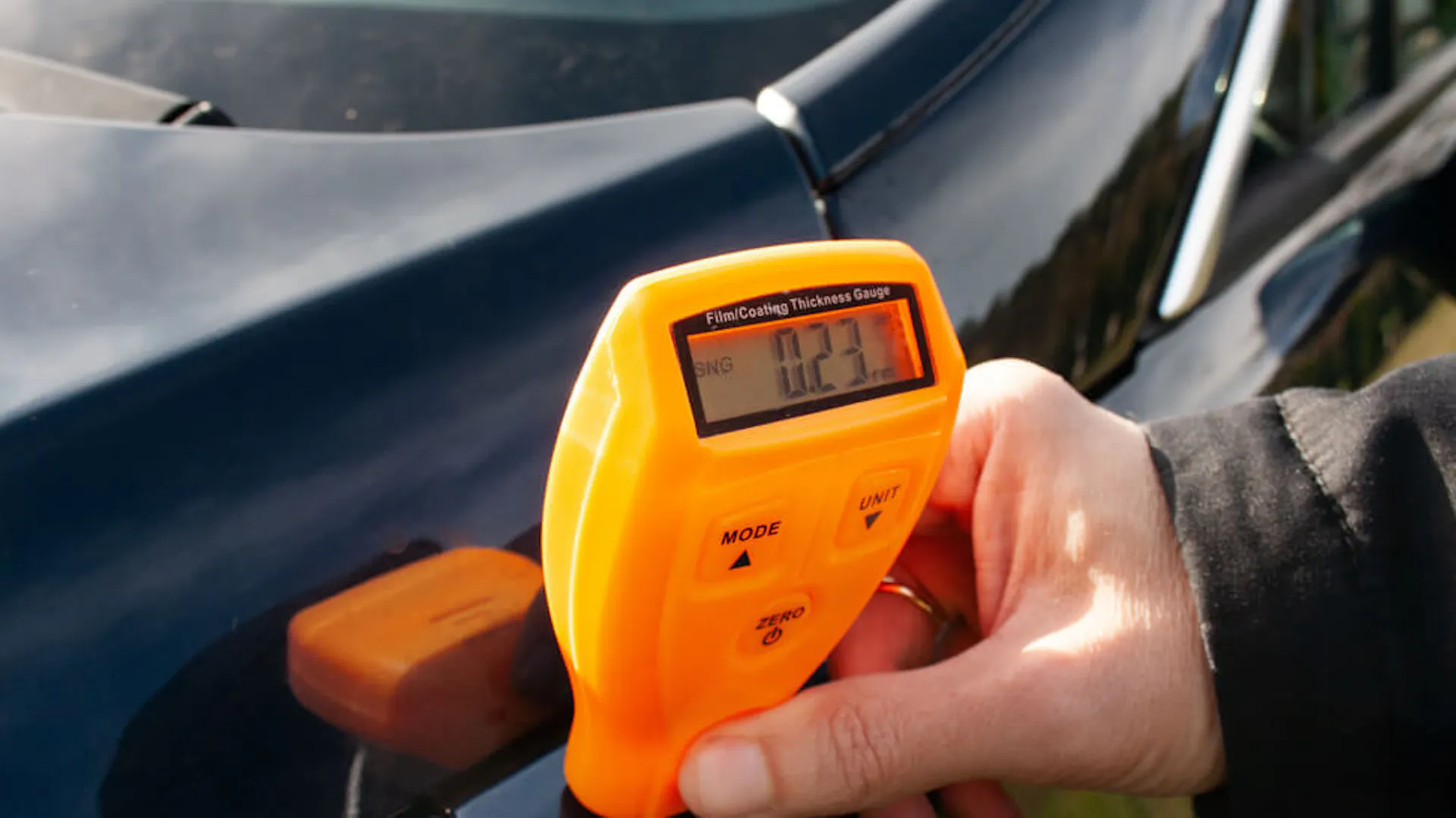 Mężczyzna używa miernika lakieru, aby sprawdzić stan karoserii