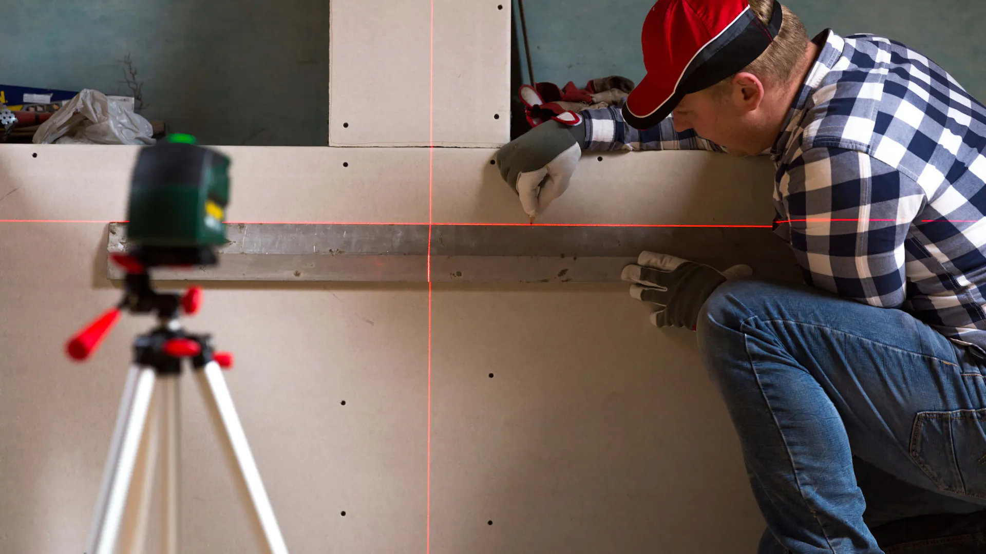 Fachowiec rysuje linię na ścianie korzystając z poziomicy laserowej.