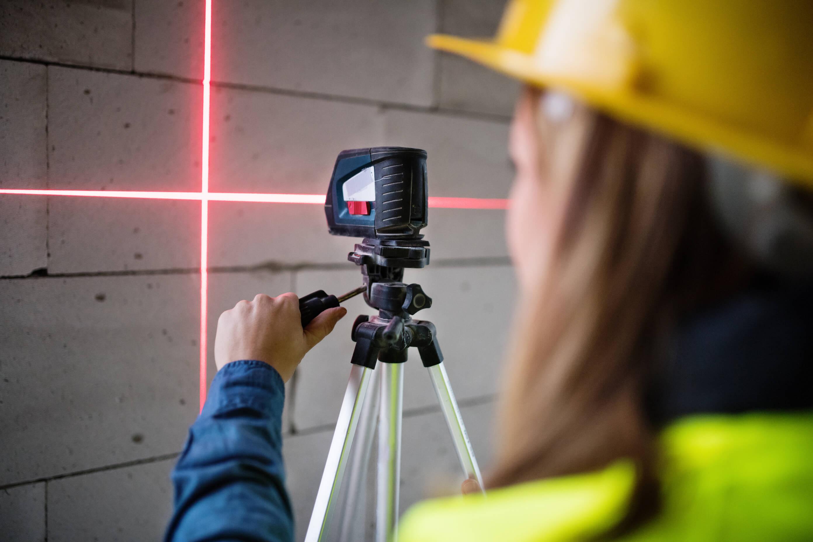 Kobieta sprawdza ściany poziomicą laserową na statywie.