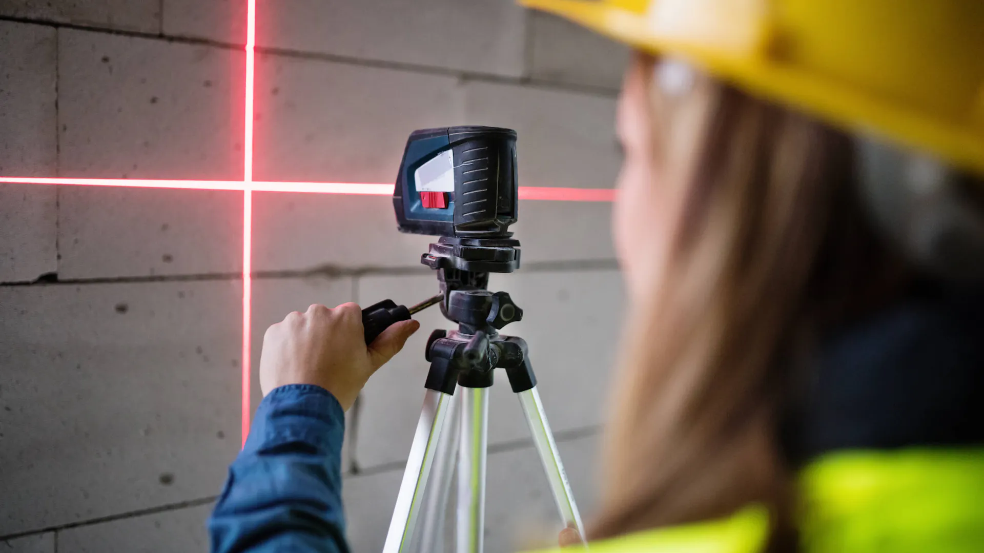 Kobieta sprawdza ściany poziomicą laserową na statywie.