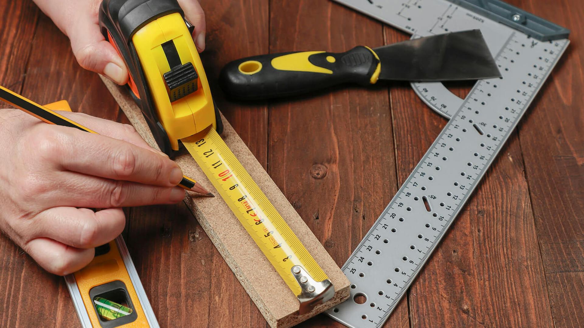 Mężczyzna używa miarki, by wymierzyć odpowiedni fragment drewna.