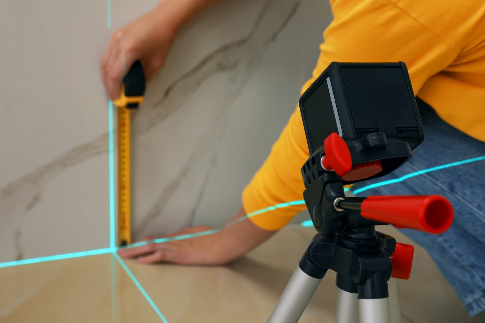 Kobieta mierzy odpowiedni kąt na ścianie poziomicą laserową i miarką.
