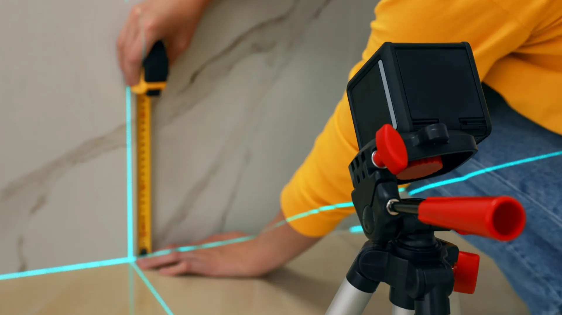 Kobieta mierzy odpowiedni kąt na ścianie poziomicą laserową i miarką.