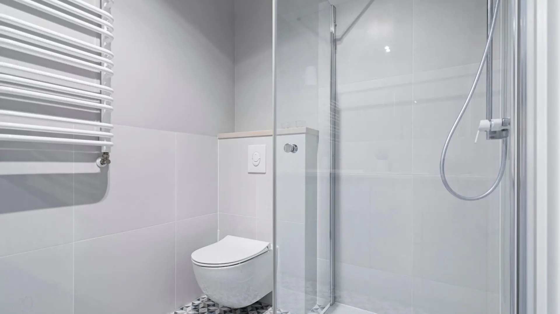 Duże jasne płytki w łazience połączone z mozaiką na podłodze.