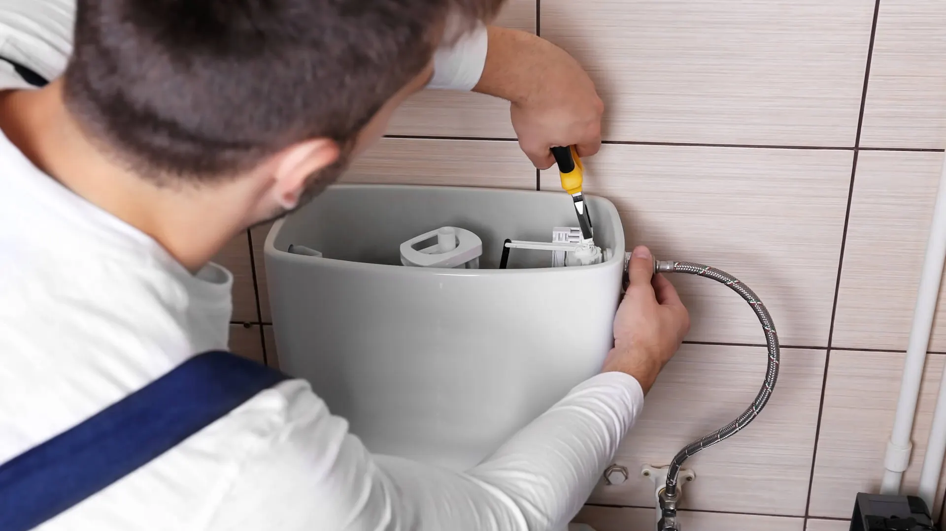 Majsterkowicz na tle ściany z zamontowanym WC podtynkowym i przyciskiem spłukującym w łazience wyłożonej szarymi płytkami