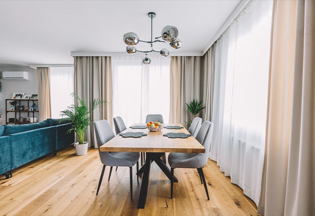 Nowoczesna jadalnia połączona z salonem. Drewniany, loftowy stół, wokół szare krzesła tapicerowane.