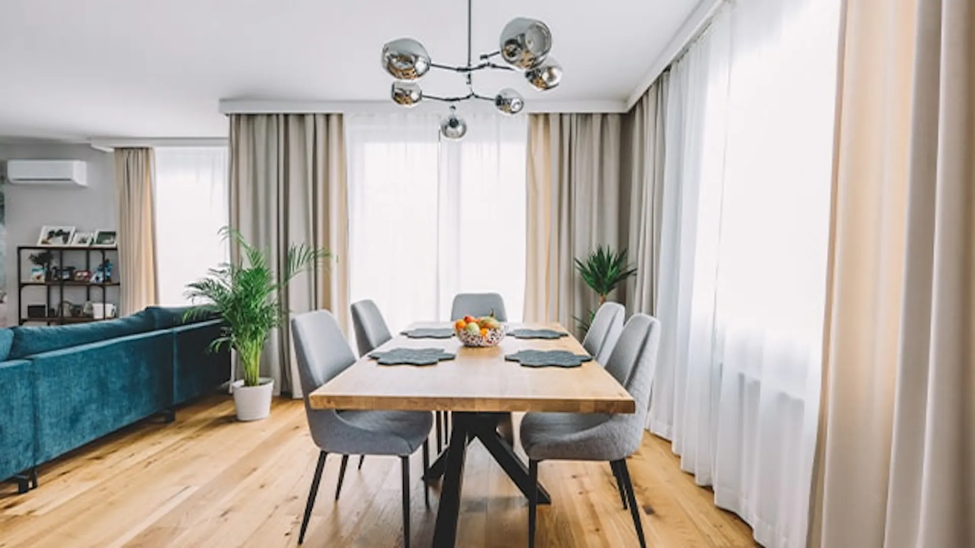 Nowoczesna jadalnia połączona z salonem. Drewniany, loftowy stół, wokół szare krzesła tapicerowane.