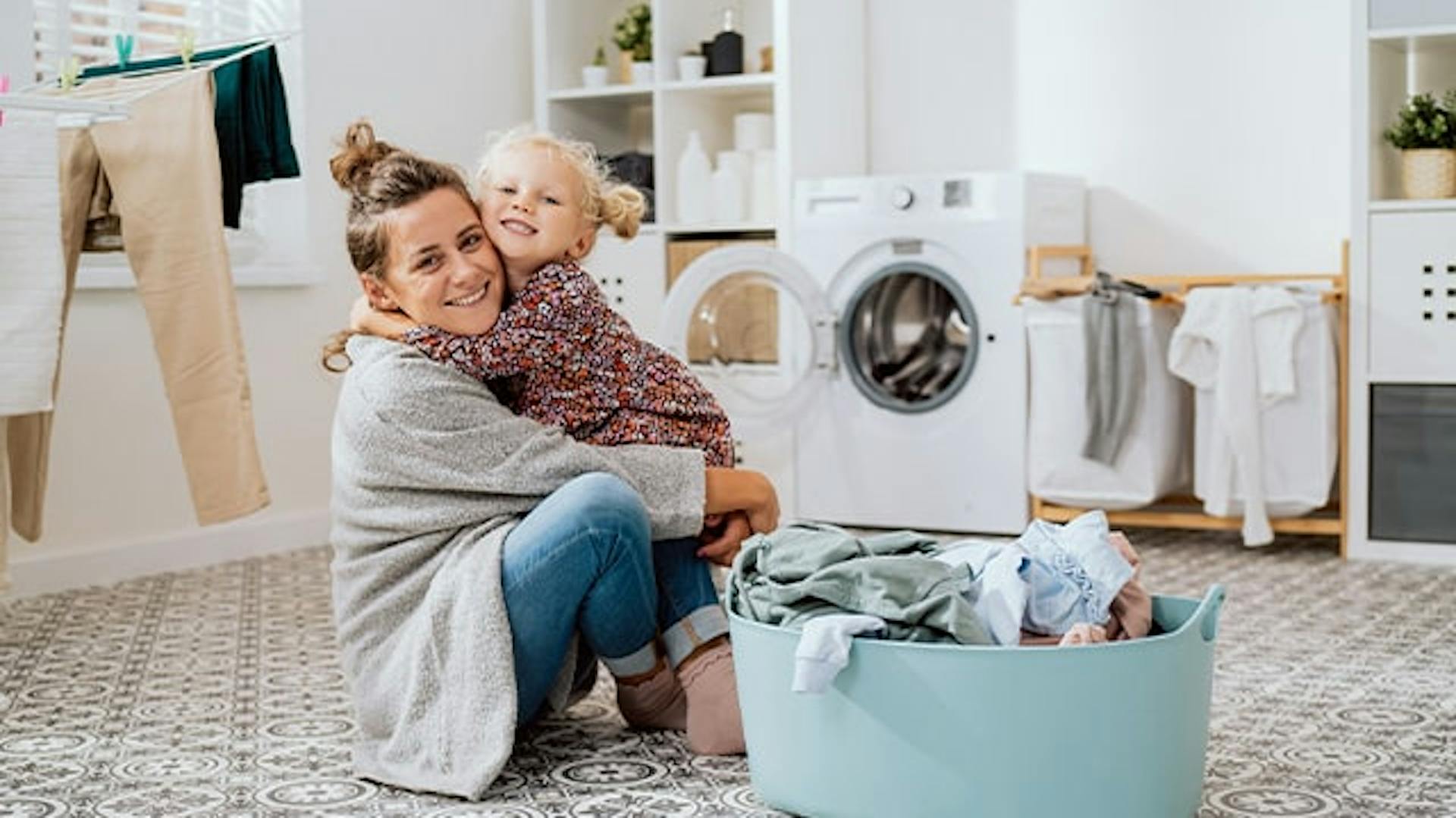 Kobieta z małą dziewczyną na podłodze w pralni. Obok kosz z praniem.