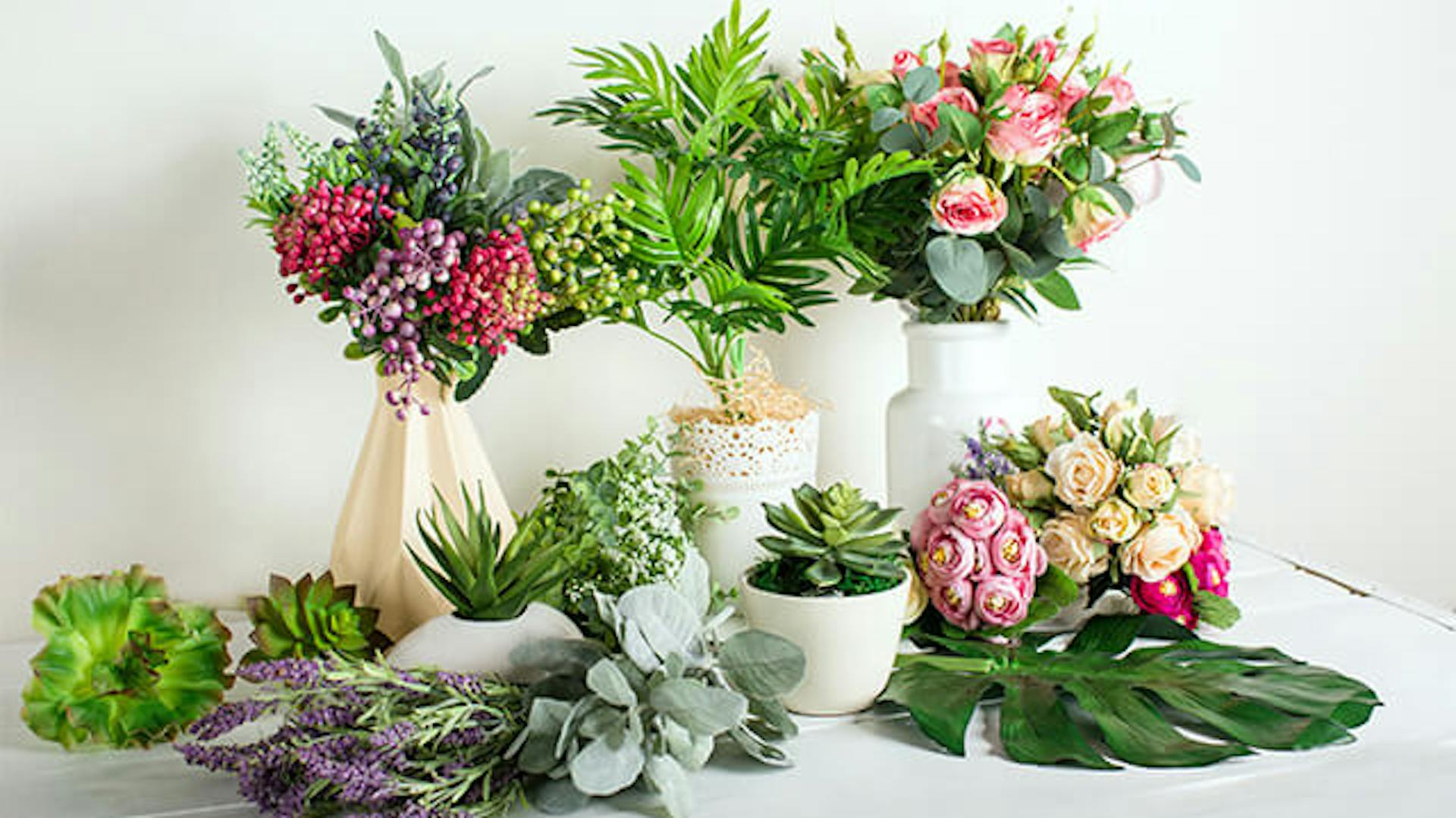 Wazony ze sztucznymi kwiatami. Obok doniczki ze sztucznymi sukulentami.