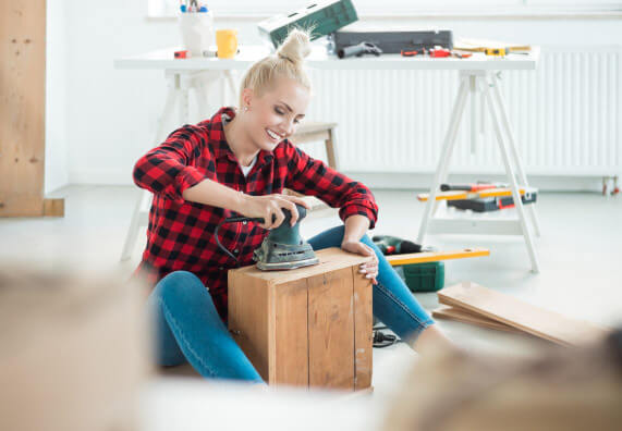 Kobieta szlifuje drewniany mebel wykonując w domu projekt DIY