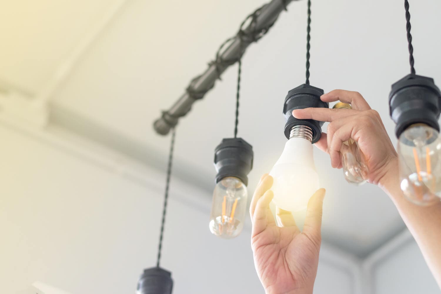 Mężczyzna montuje żarówkę energooszczędną do lampy sufitowej.