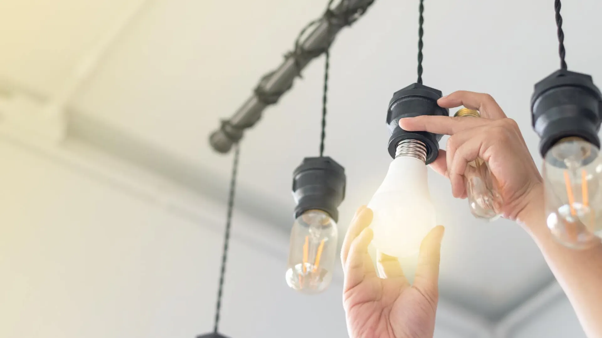 Mężczyzna montuje żarówkę energooszczędną do lampy sufitowej.