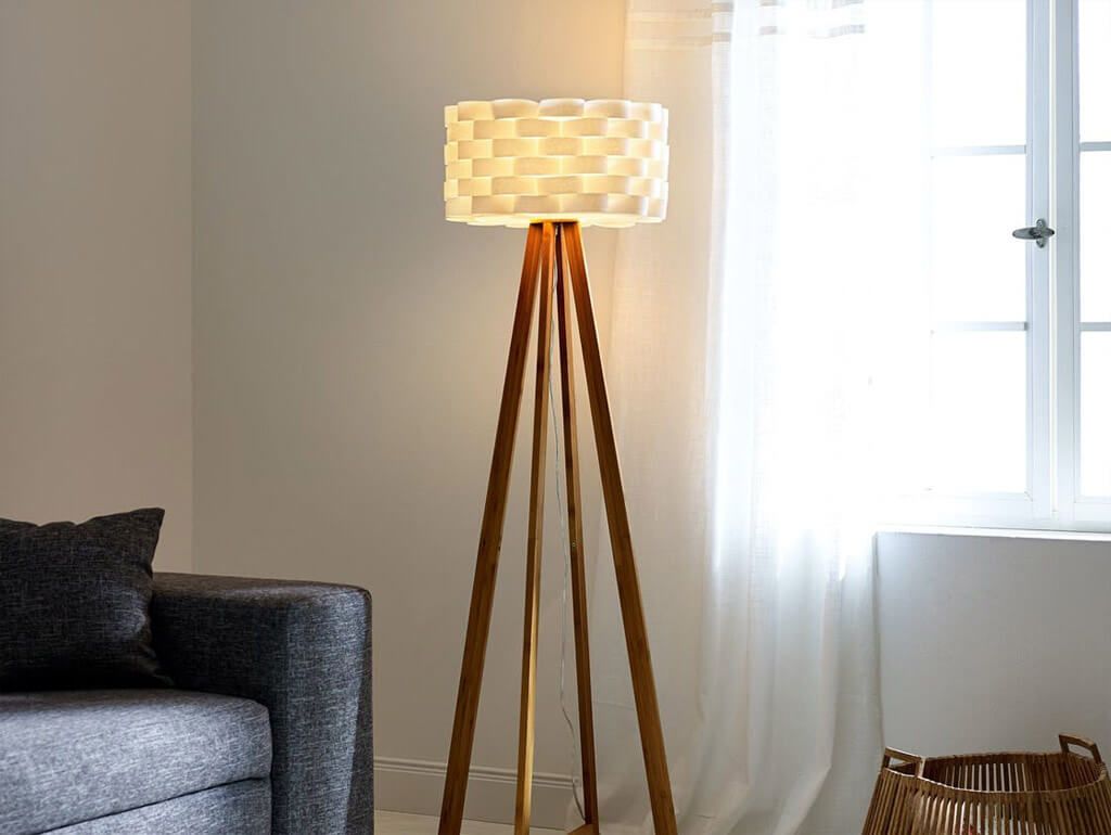 Lampa stojąca w salonie, po lewej szara kanapa, po prawej okno.