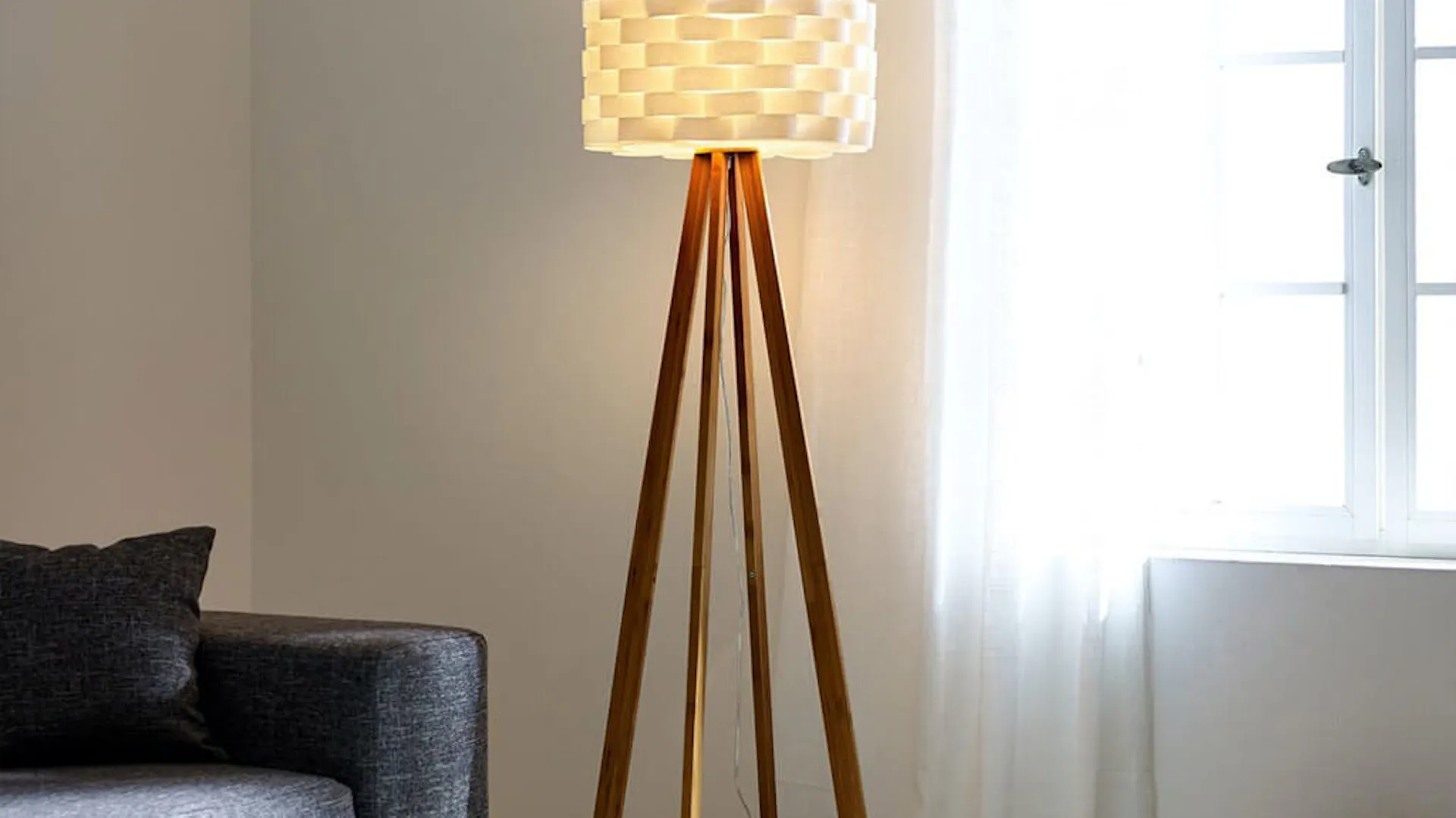 Lampa stojąca w salonie, po lewej szara kanapa, po prawej okno.