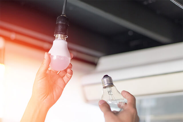 Kobieta wymienia starą żarówkę na energooszczędną lampę LED.
